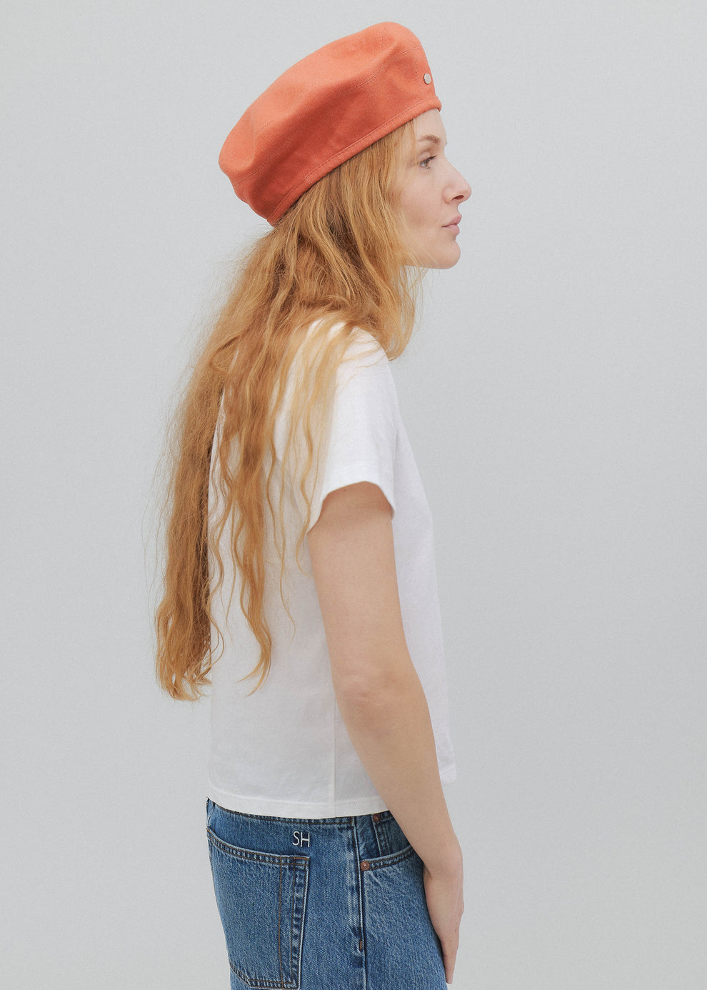 Person wearing a white t-shirt, blue jeans, and an orange beret against a plain background