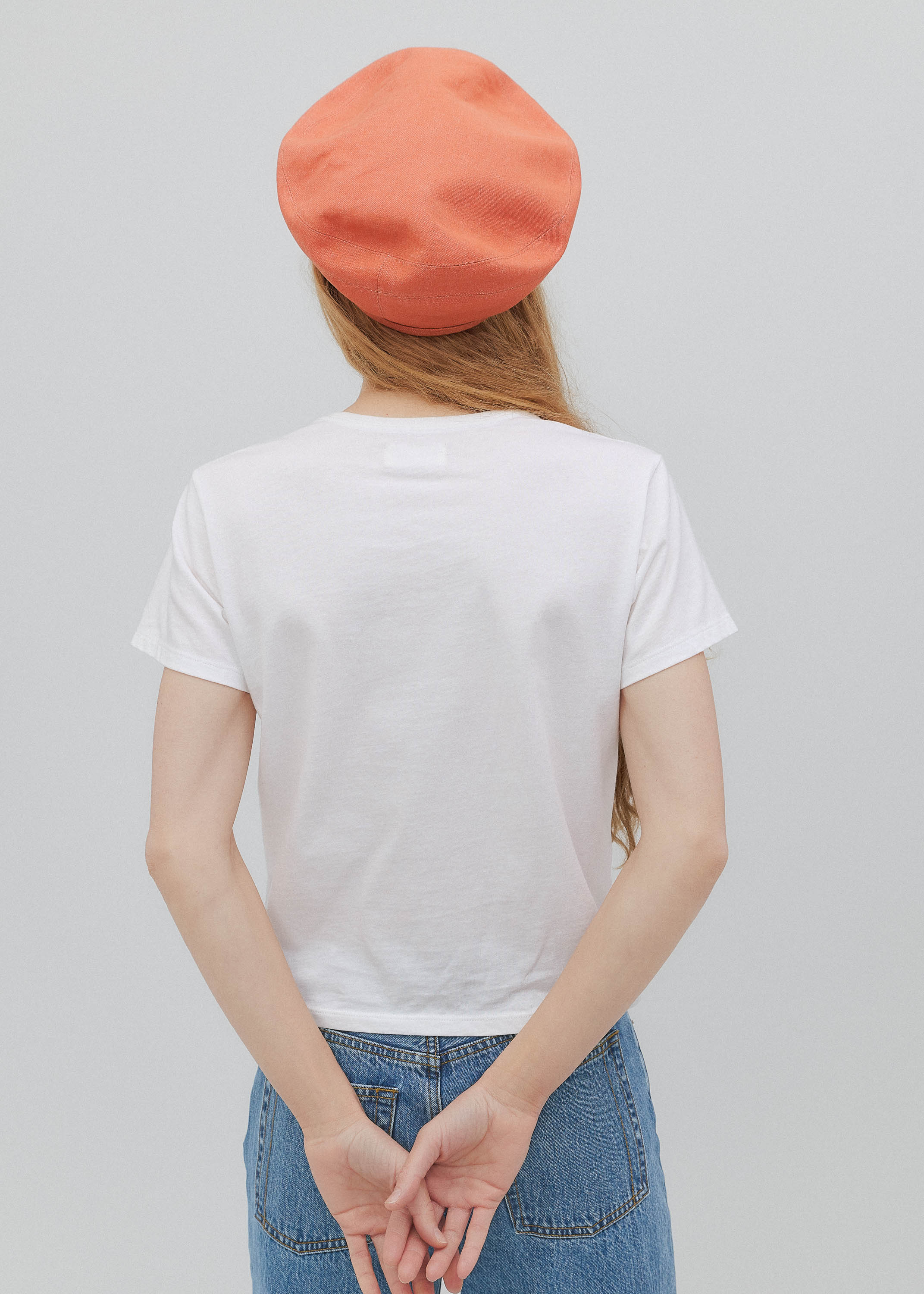 Person wearing a white t-shirt, blue jeans, and an orange beret on a plain background