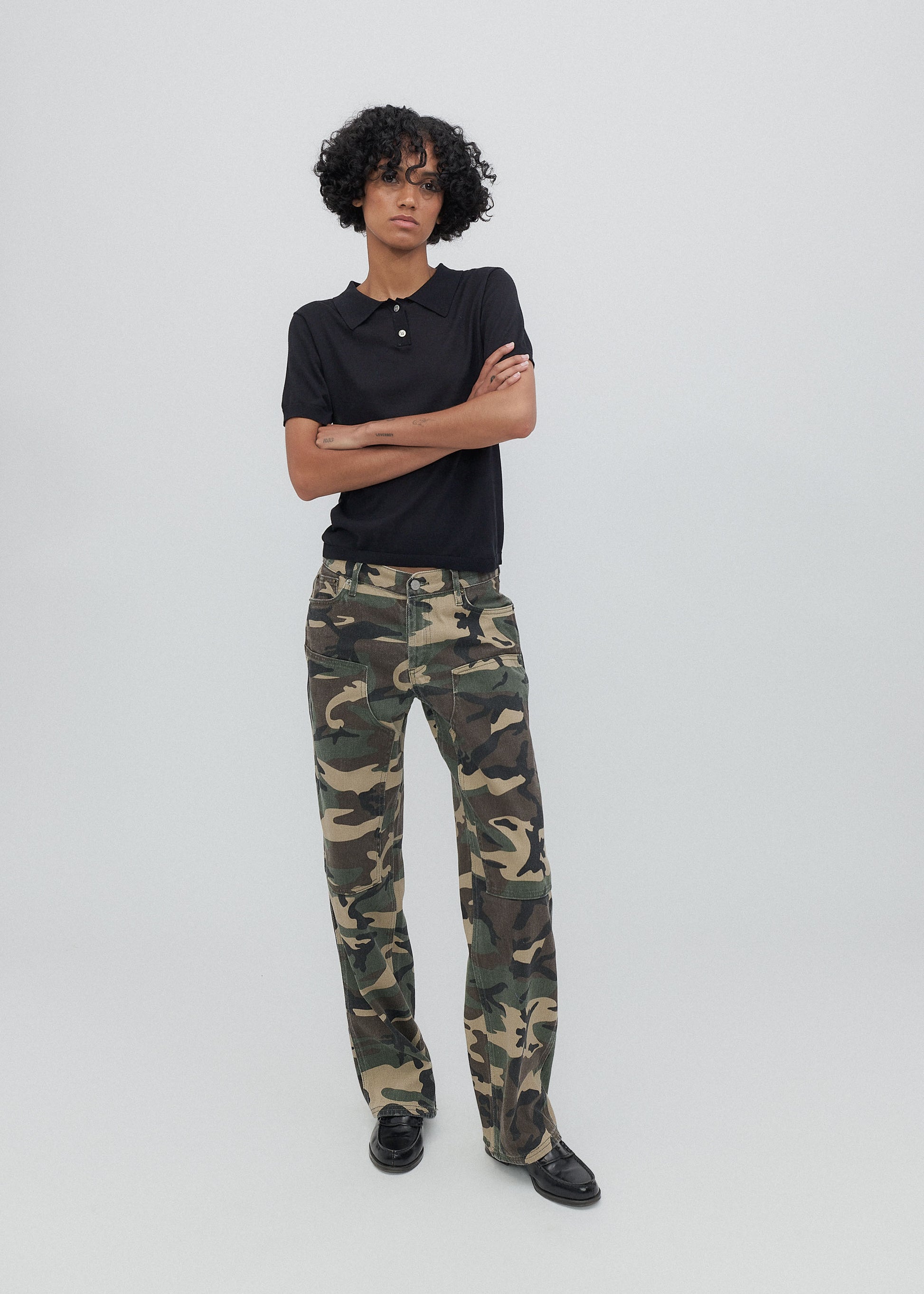Person wearing a black polo shirt and camouflage pants on a white background