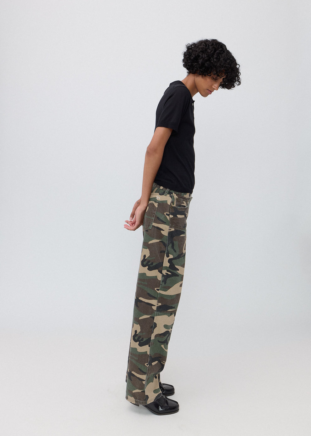 Person wearing camouflage pants and a black shirt on a white background