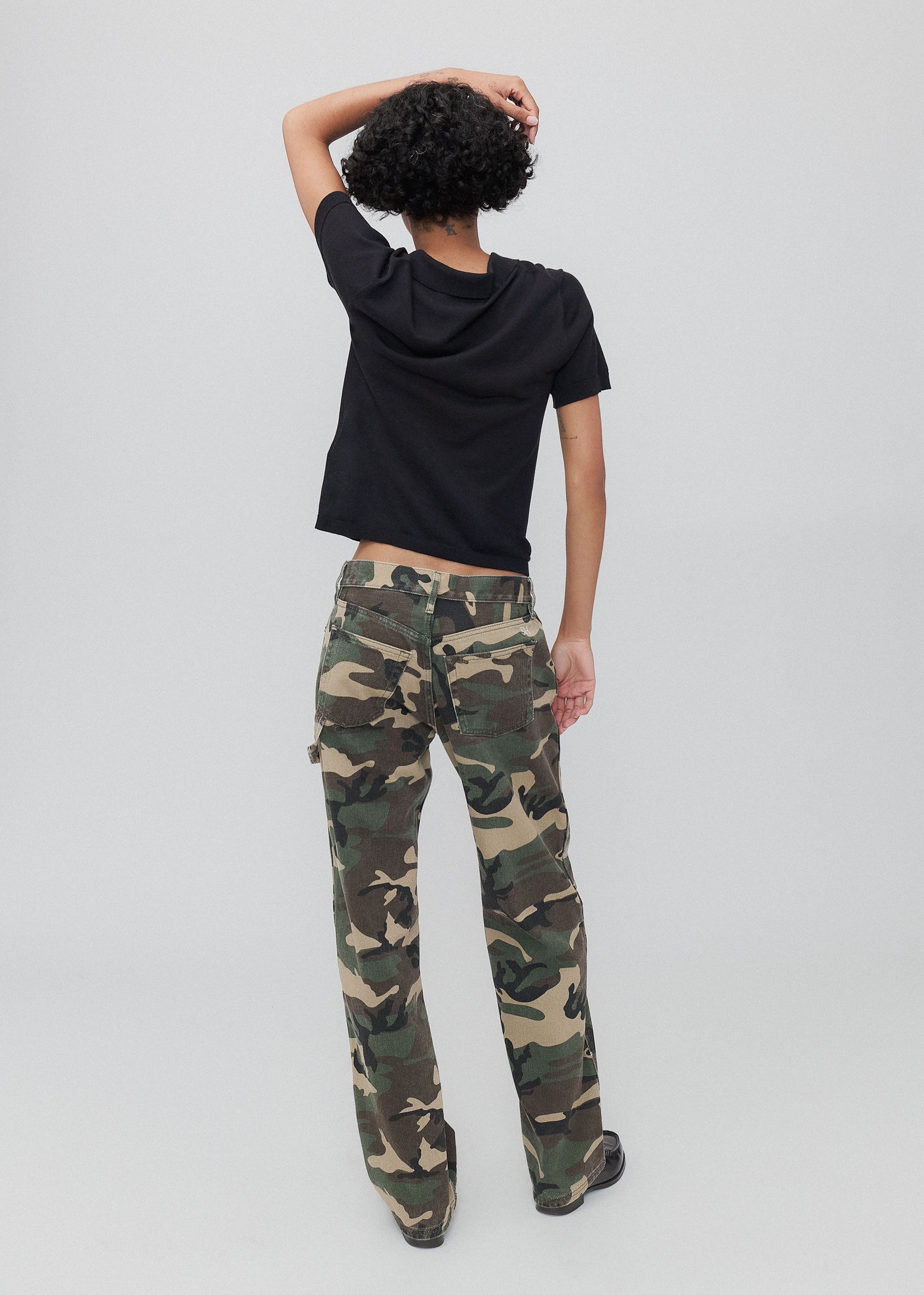 Person wearing camouflage pants and a black shirt on a white background