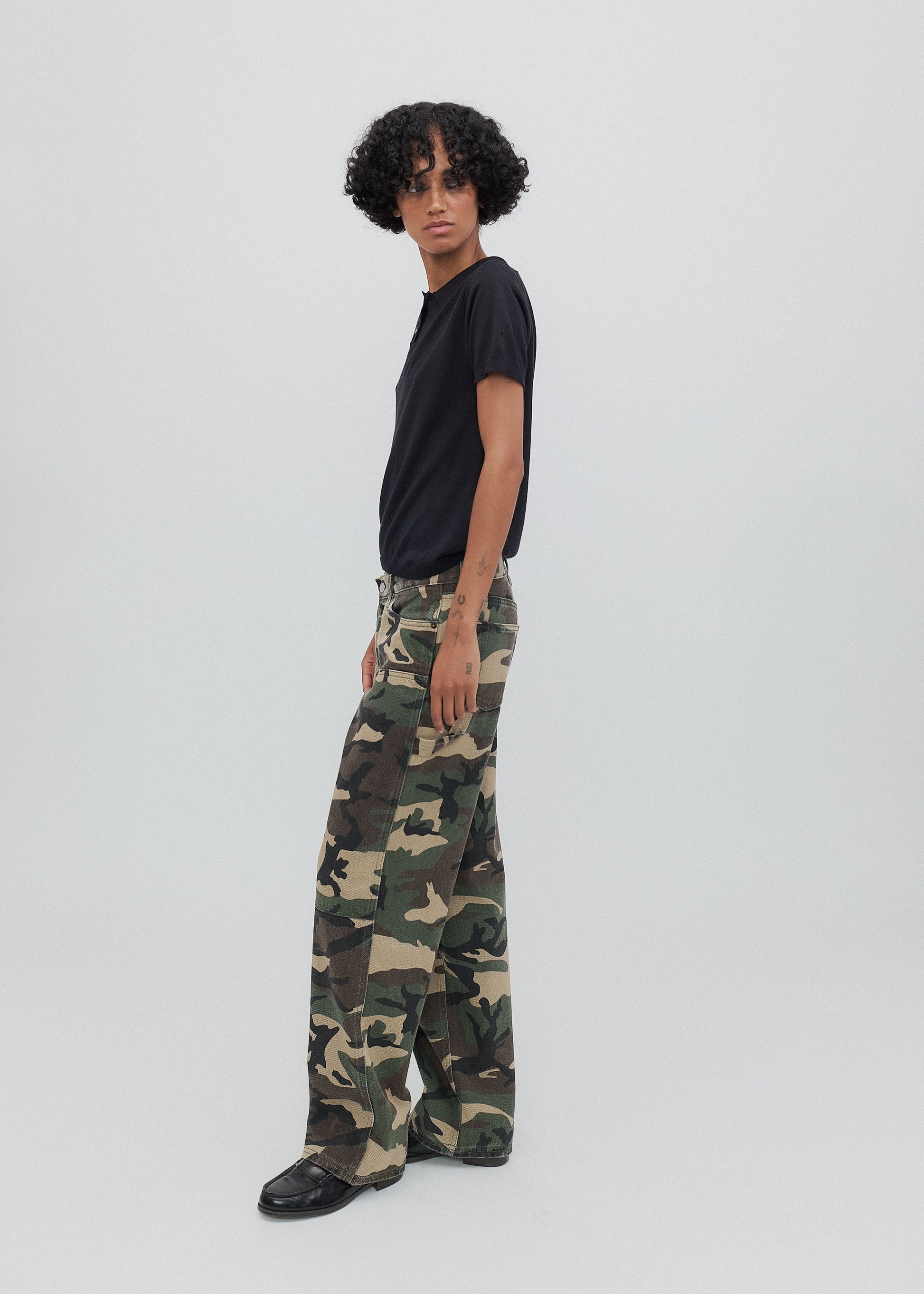 Person wearing camouflage pants and a black shirt on a white background