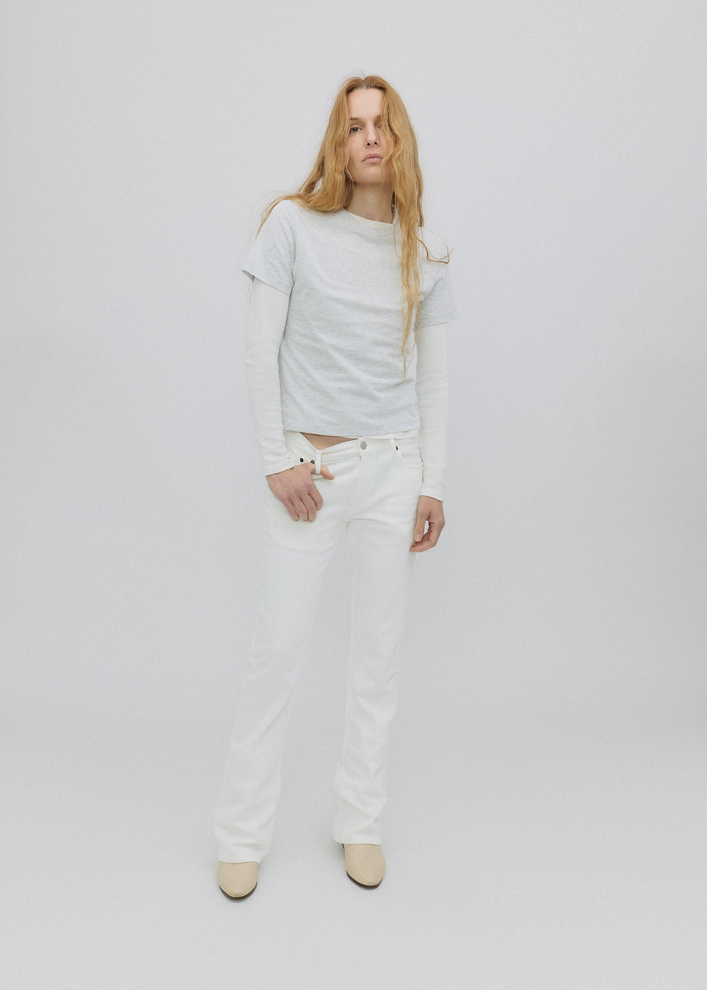 Person wearing a light gray sweatshirt and white pants on a plain background