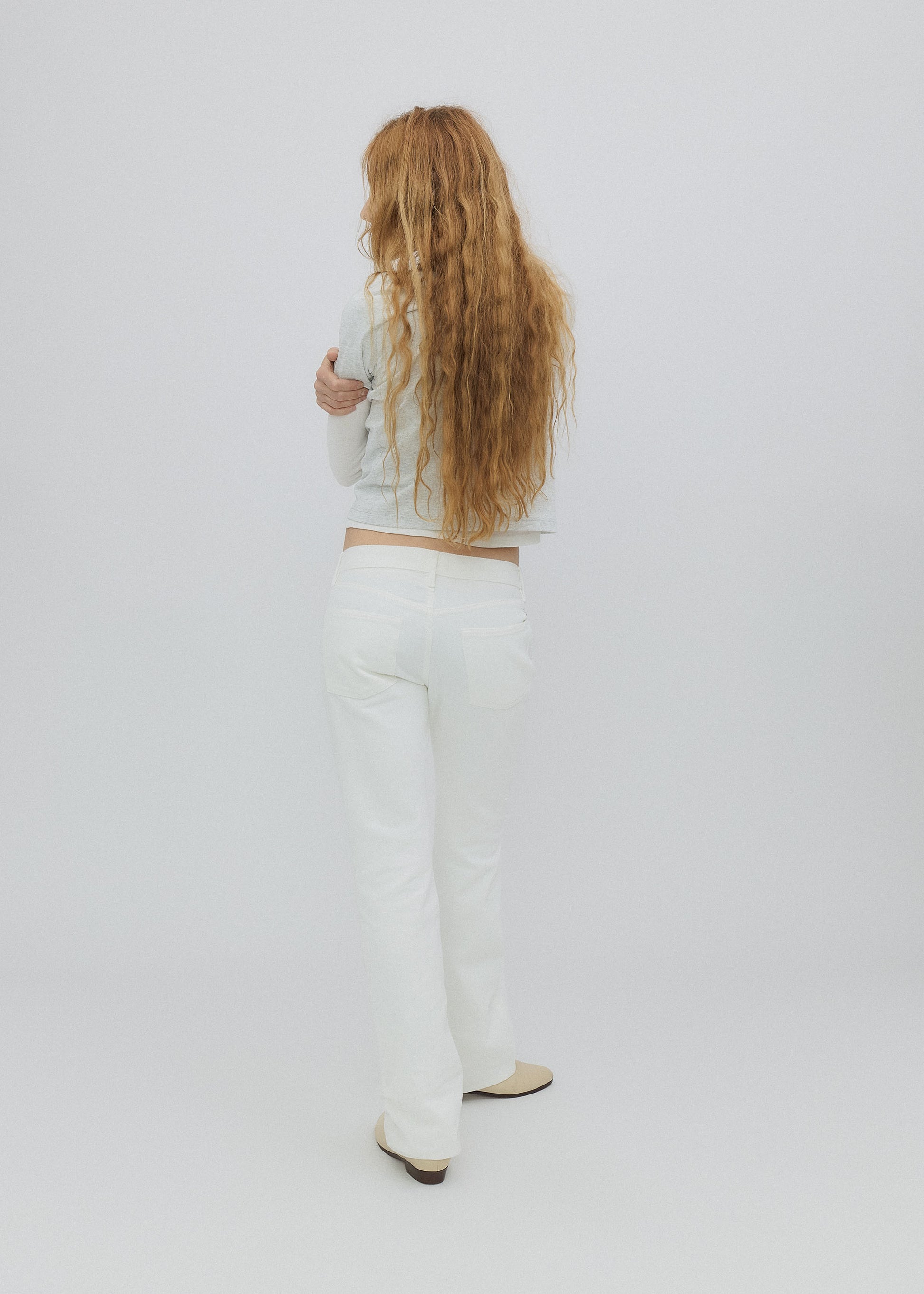 Person with long hair wearing a light-colored top and pants on a white background