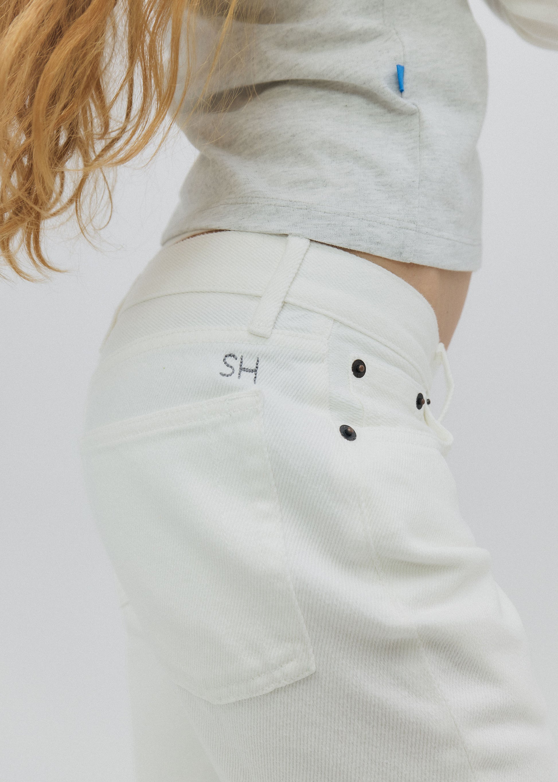 White pants with black buttons and 'SH' logo on a white background