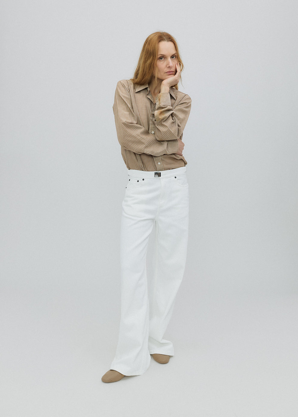 Woman wearing a beige jacket and white pants on a light gray background