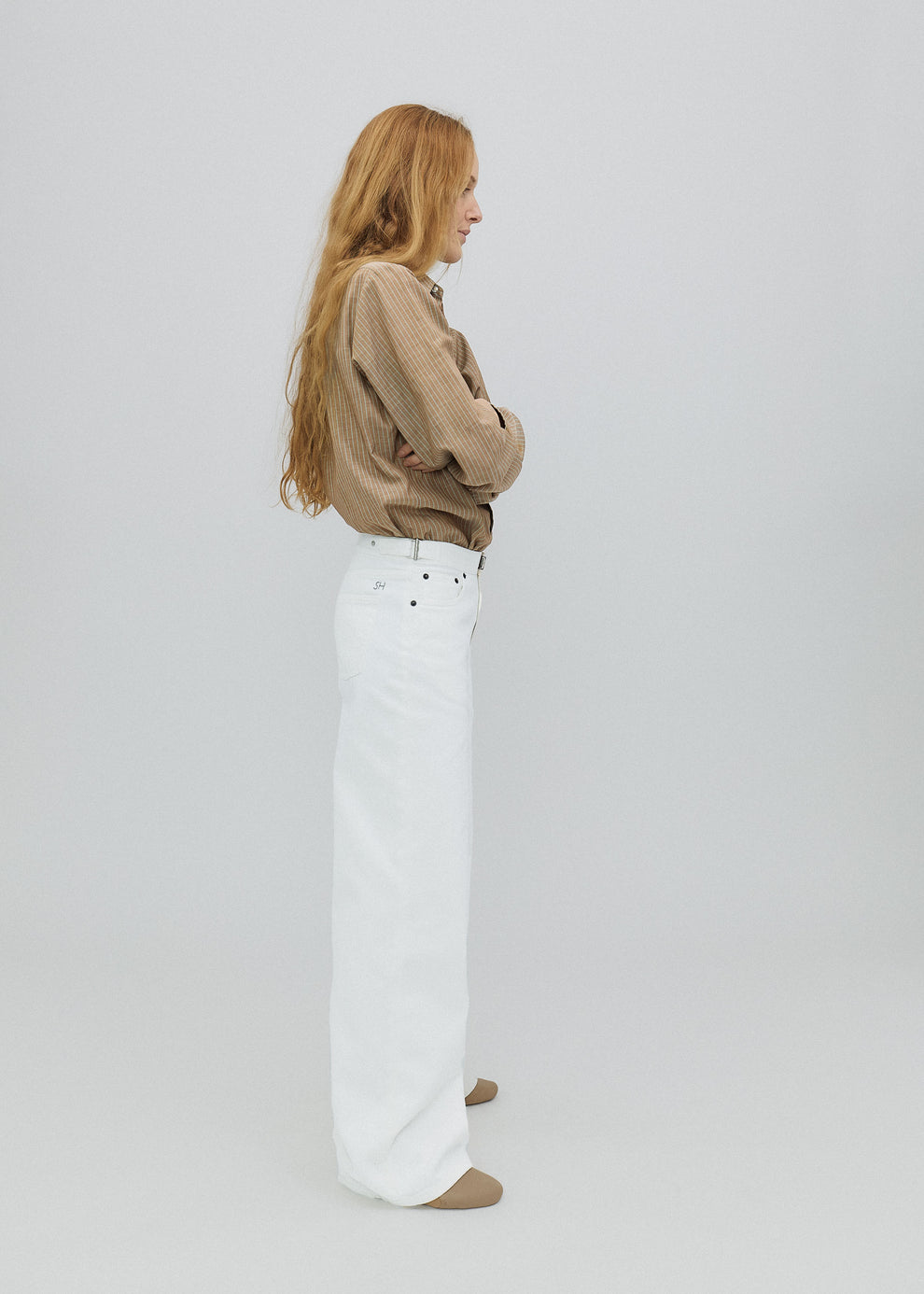 Woman wearing a beige sweater and white pants on a plain background