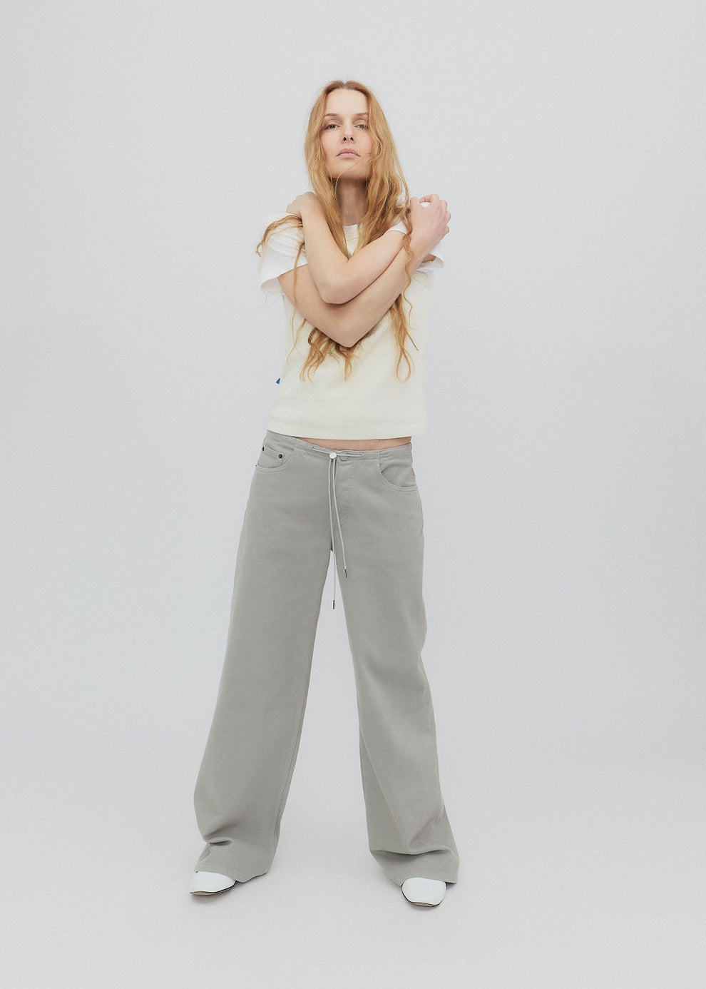 Woman wearing a white top and light gray pants on a plain background