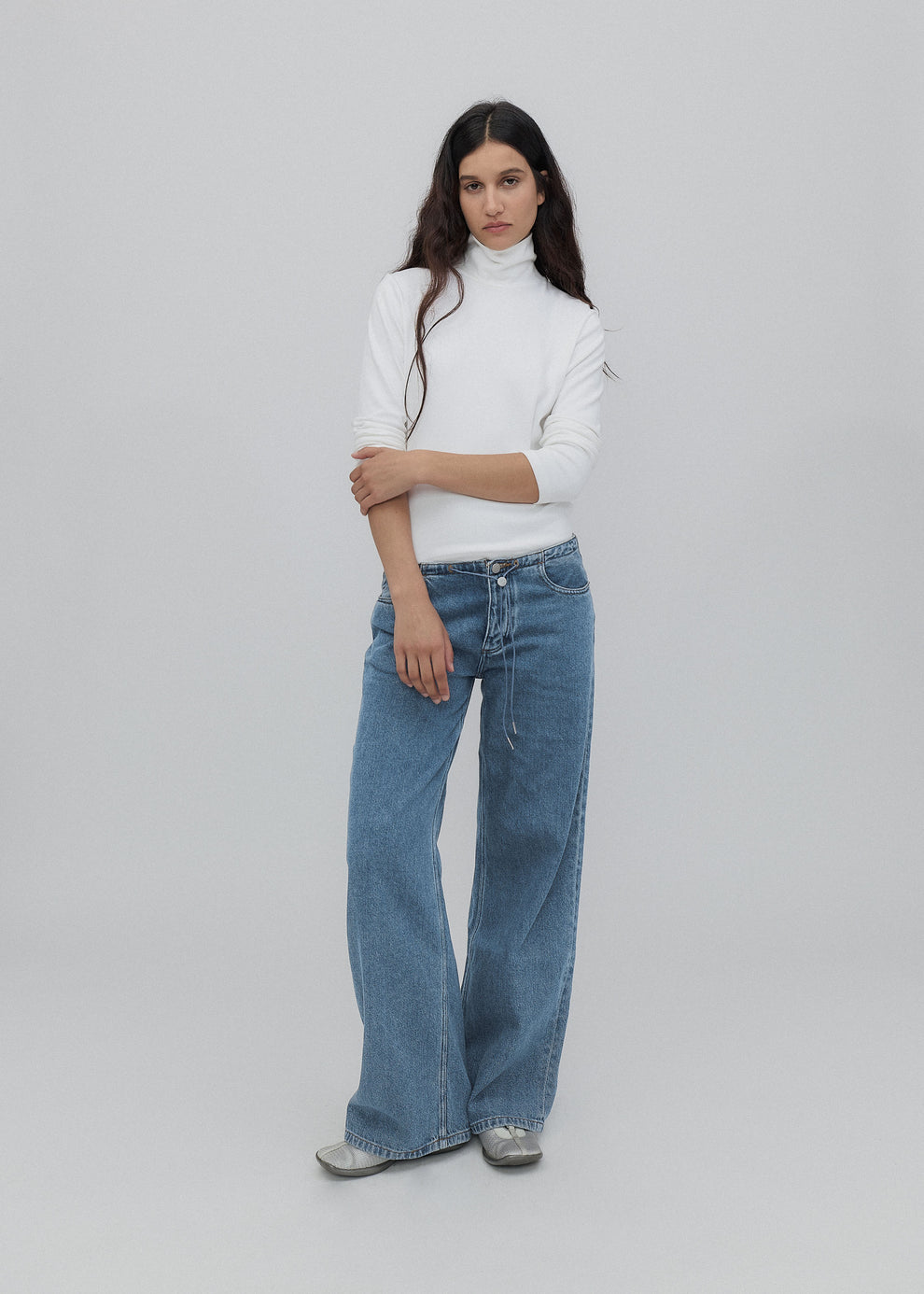 Woman wearing a white turtleneck and blue jeans on a plain background