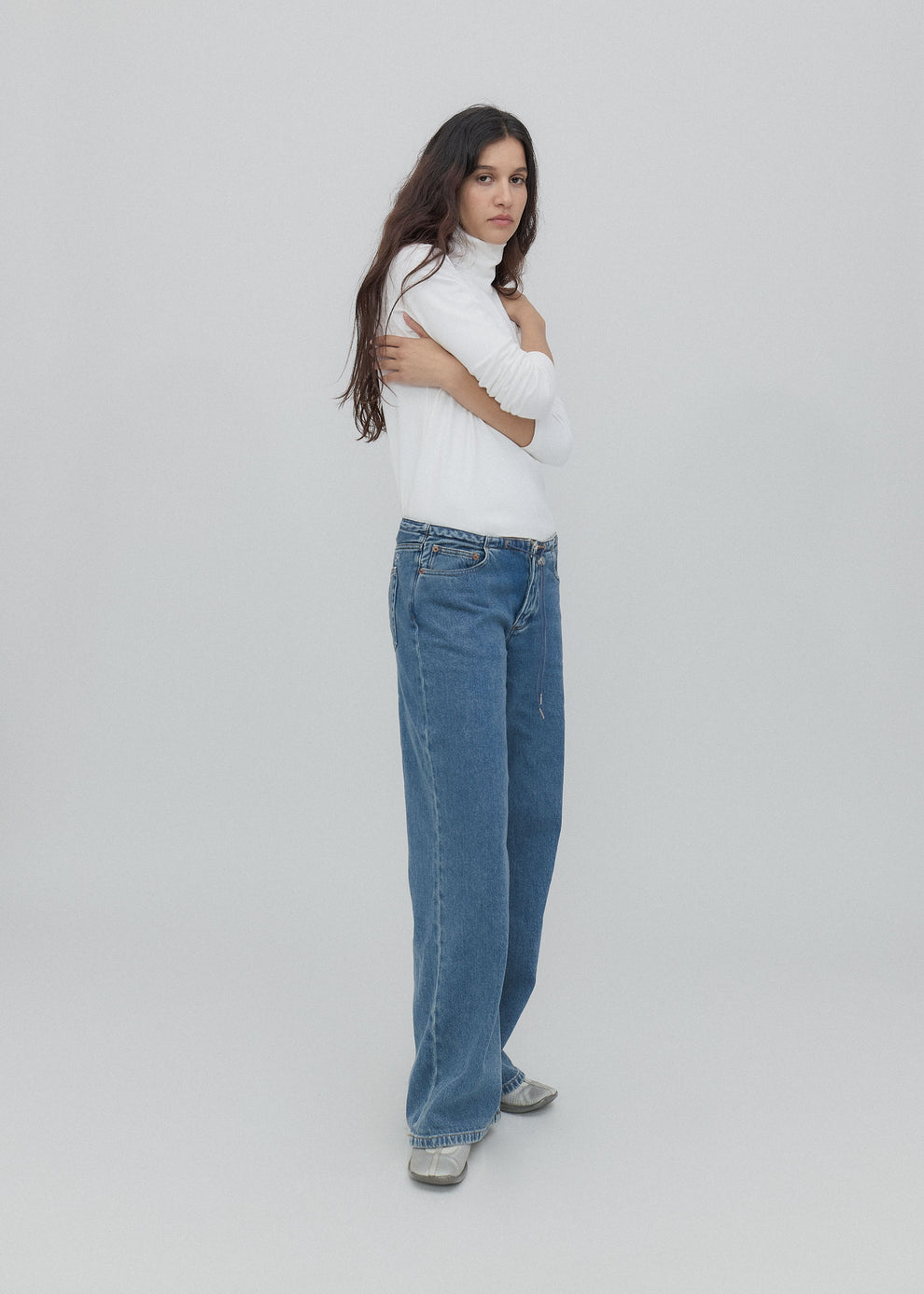 Woman wearing a white turtleneck and blue jeans on a light gray background