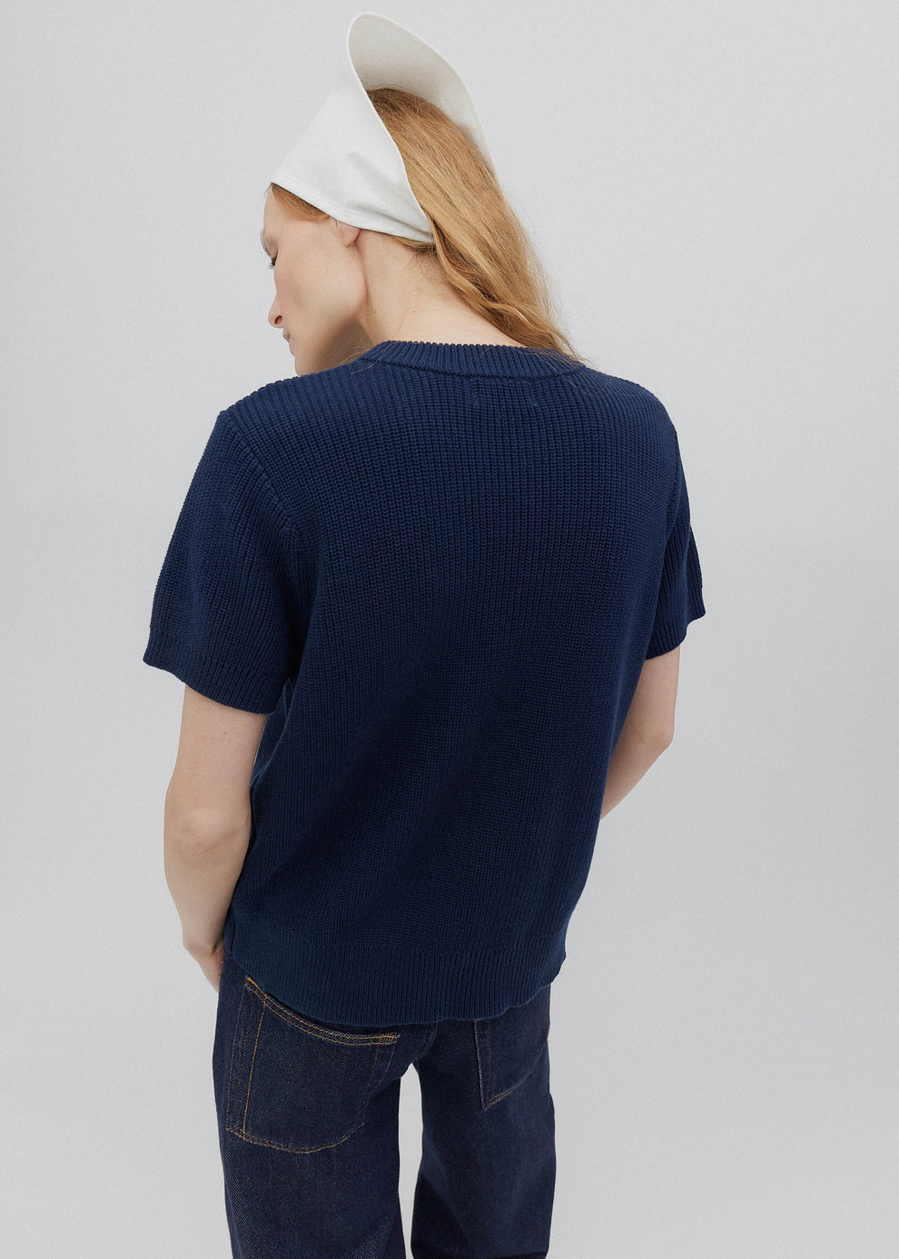 Person wearing a navy blue sweater and jeans on a plain background