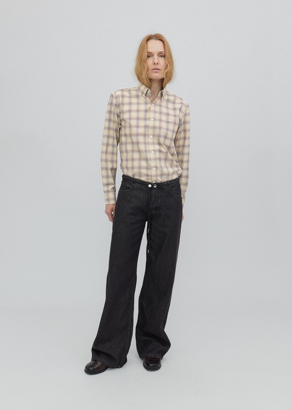 Person wearing a plaid shirt and black pants on a plain background