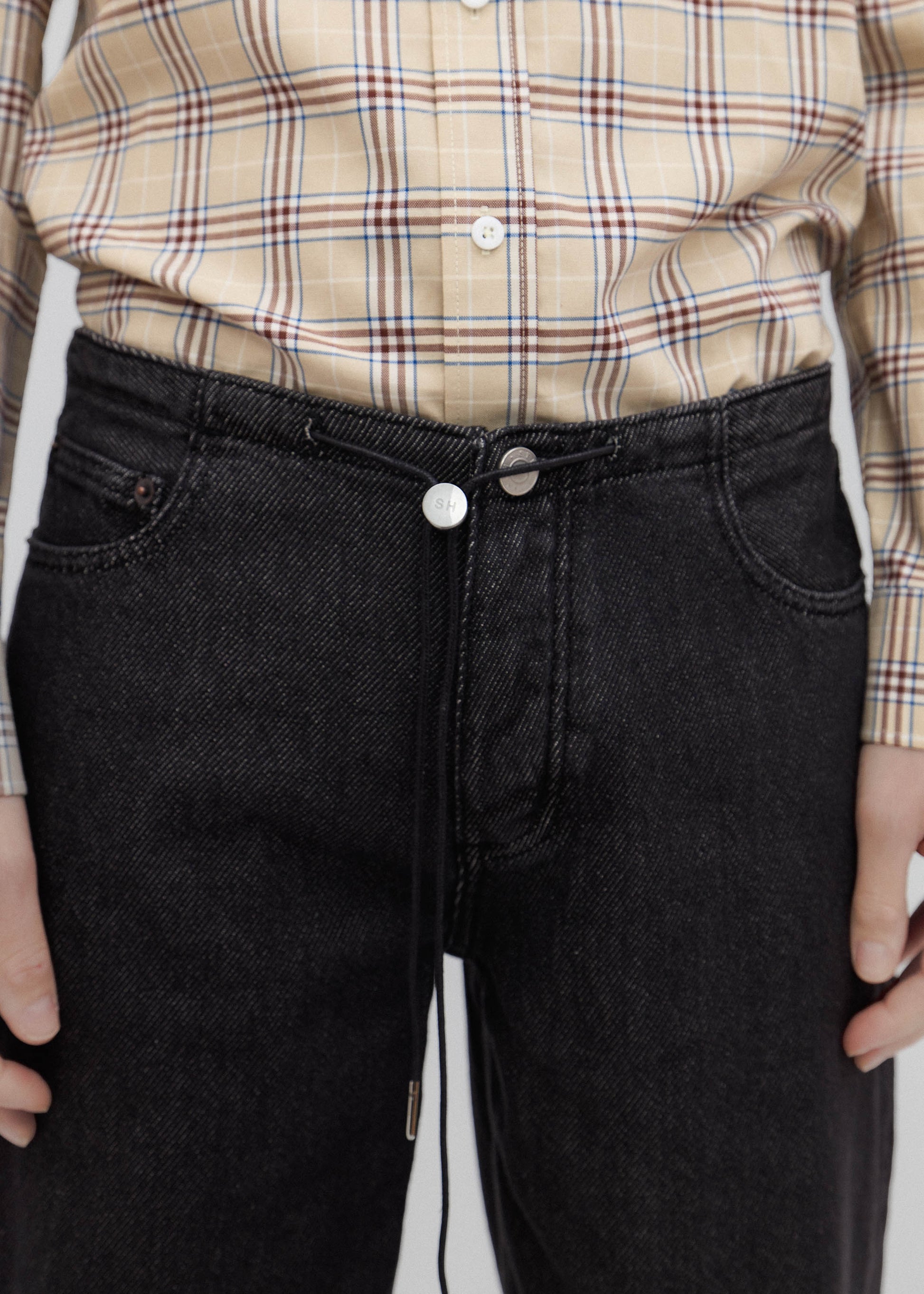 Person wearing a plaid shirt and black jeans with a white background
