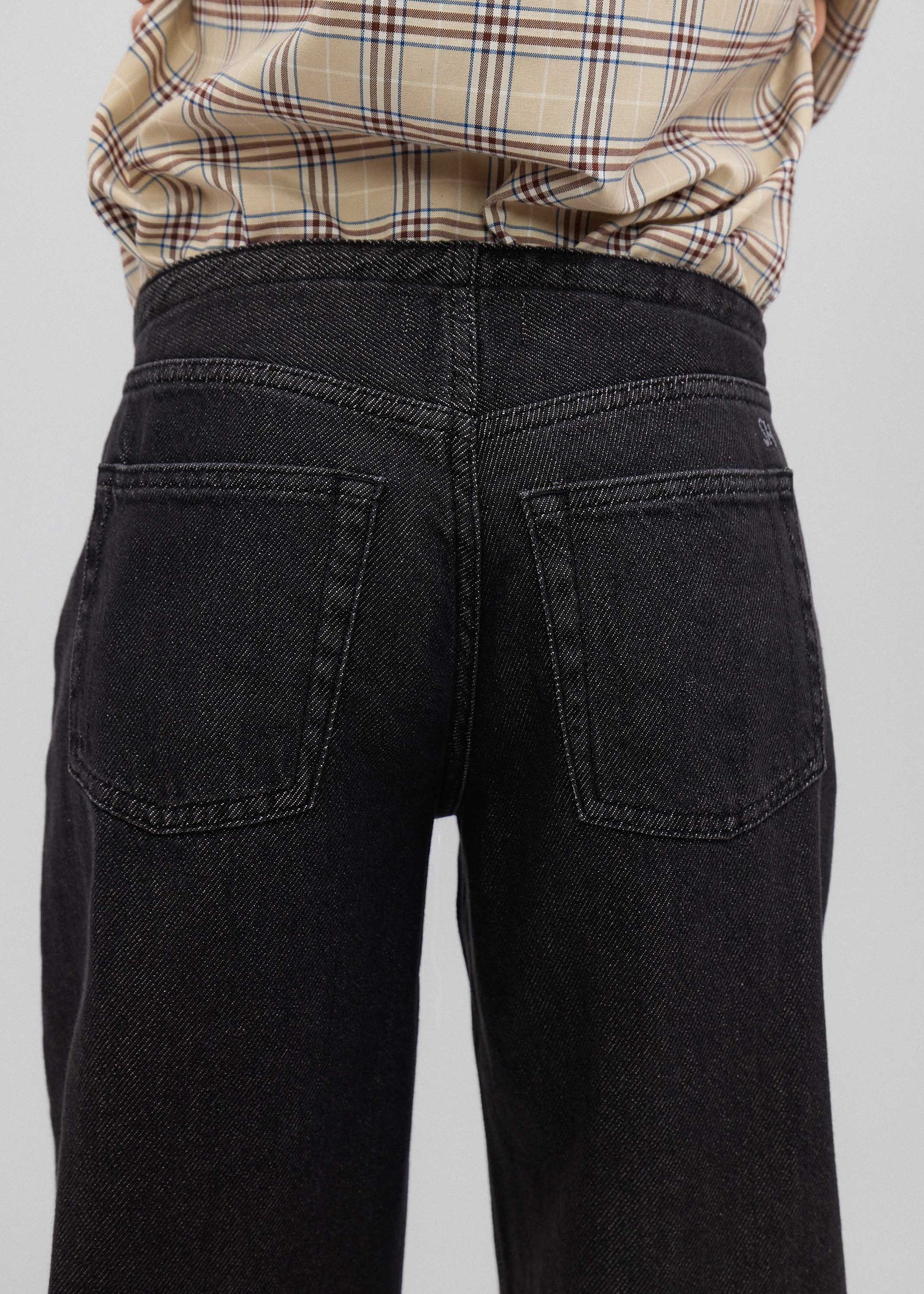 Black jeans worn by a person with a plaid shirt on a light gray background