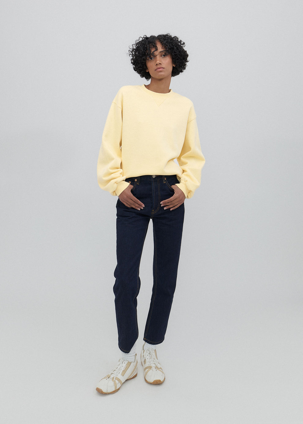 Person wearing a yellow sweater and dark jeans on a gray background