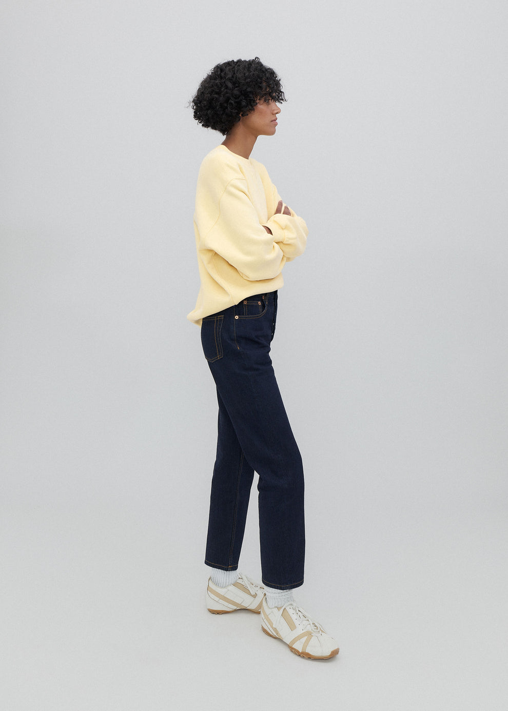 Person wearing a yellow sweater and dark jeans standing against a plain background