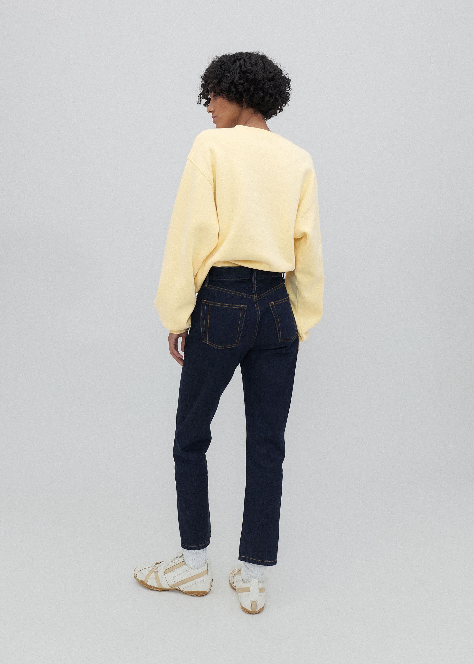 Person wearing a yellow sweater and dark jeans on a plain background
