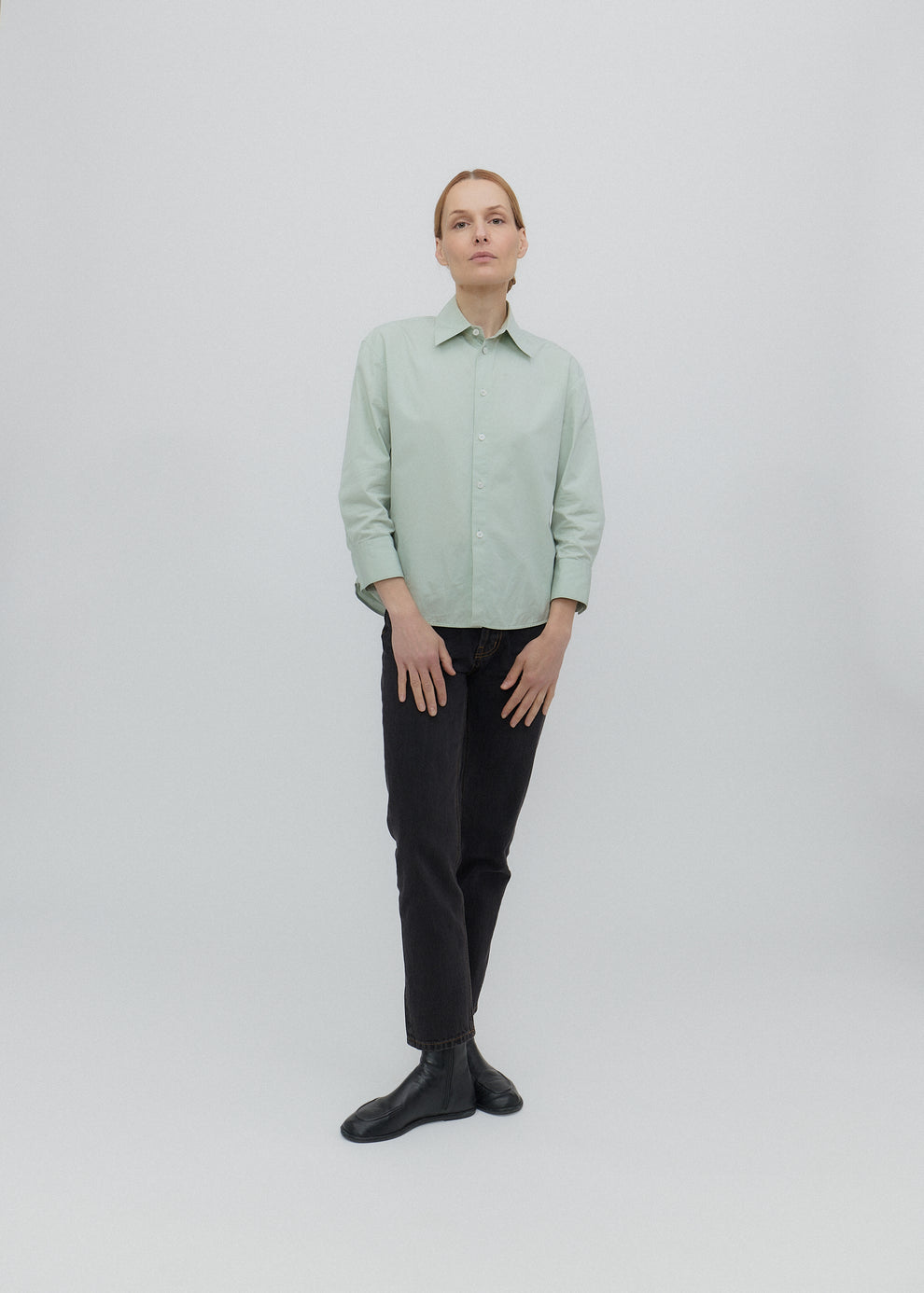 Person wearing a light green shirt and black pants on a white background