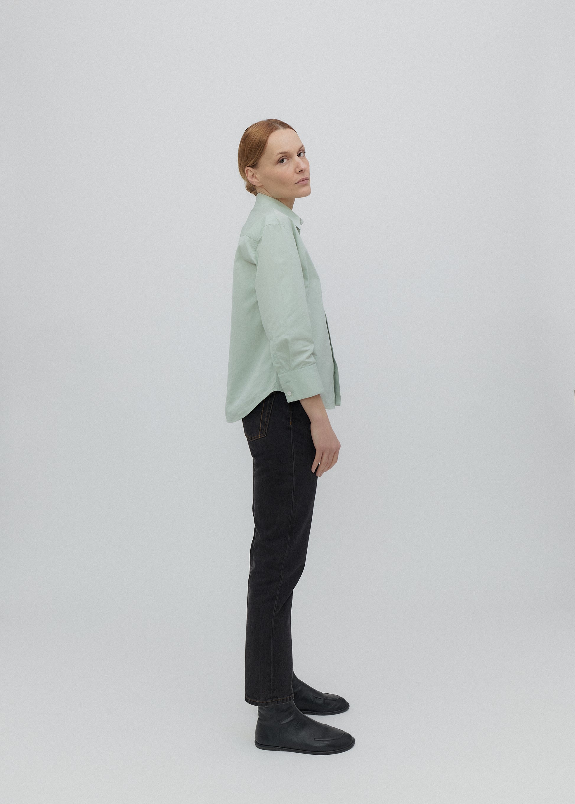 Person wearing a light green shirt and black pants on a white background