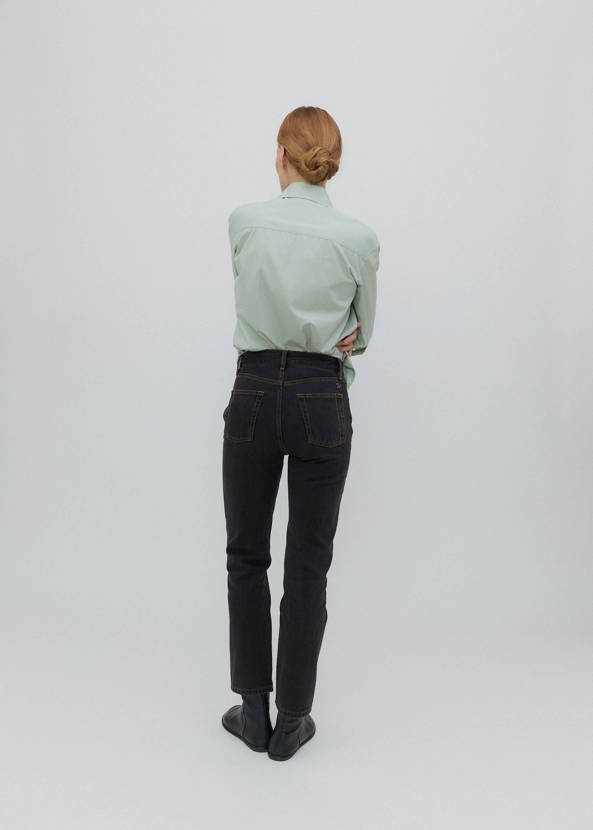 Person wearing a light green shirt and black jeans on a white background