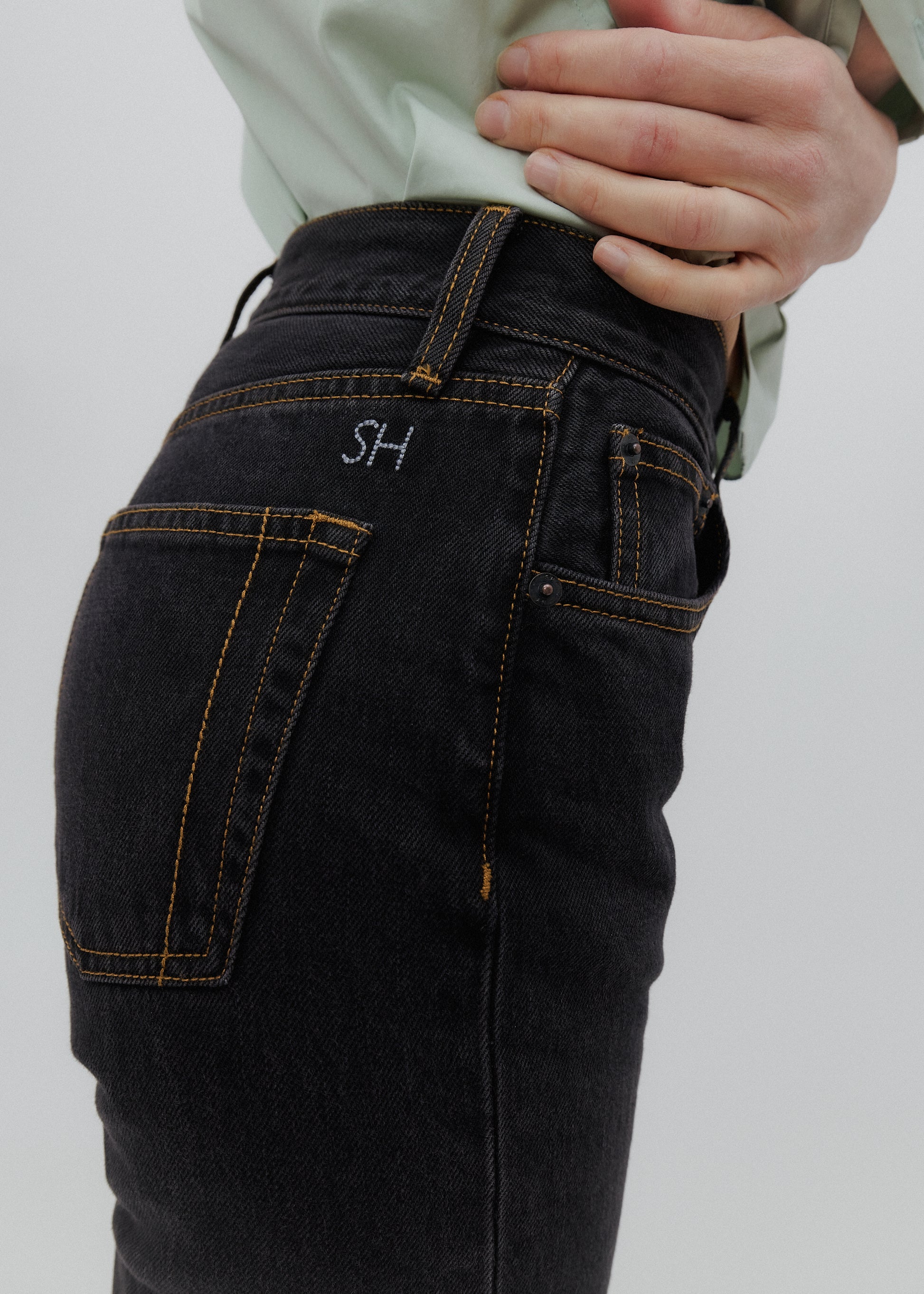 Black jeans with 'SH' logo on pocket against a light gray background