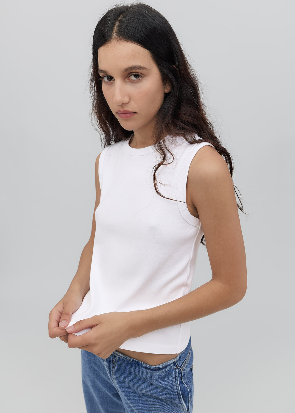 Woman wearing a white sleeveless top and blue jeans against a plain background