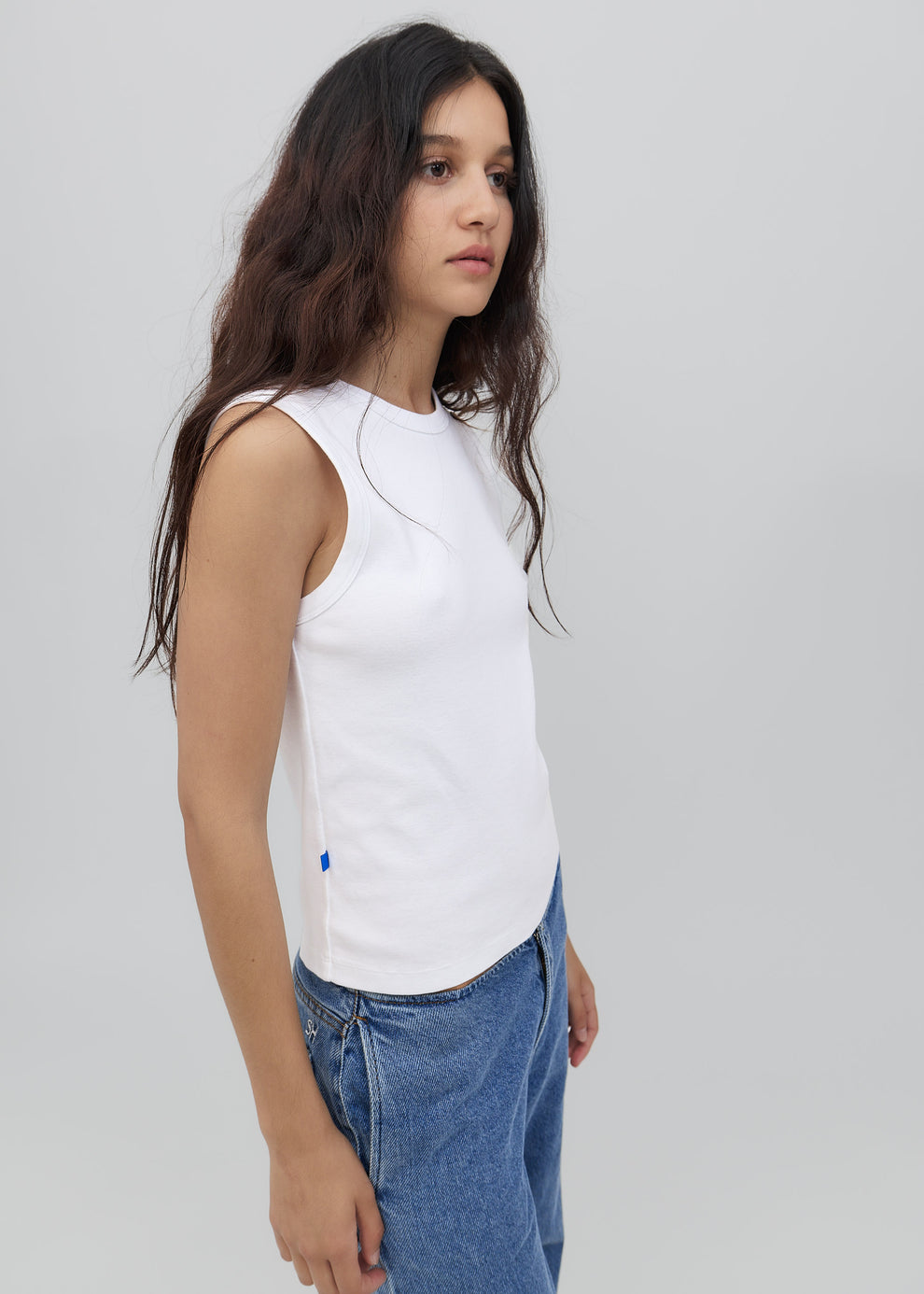 Woman wearing a white sleeveless top and blue jeans against a plain background