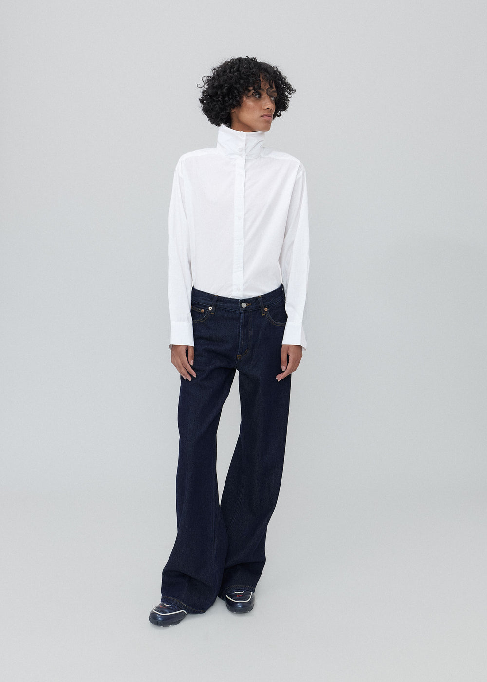 Person wearing a white blouse and dark blue jeans on a light gray background