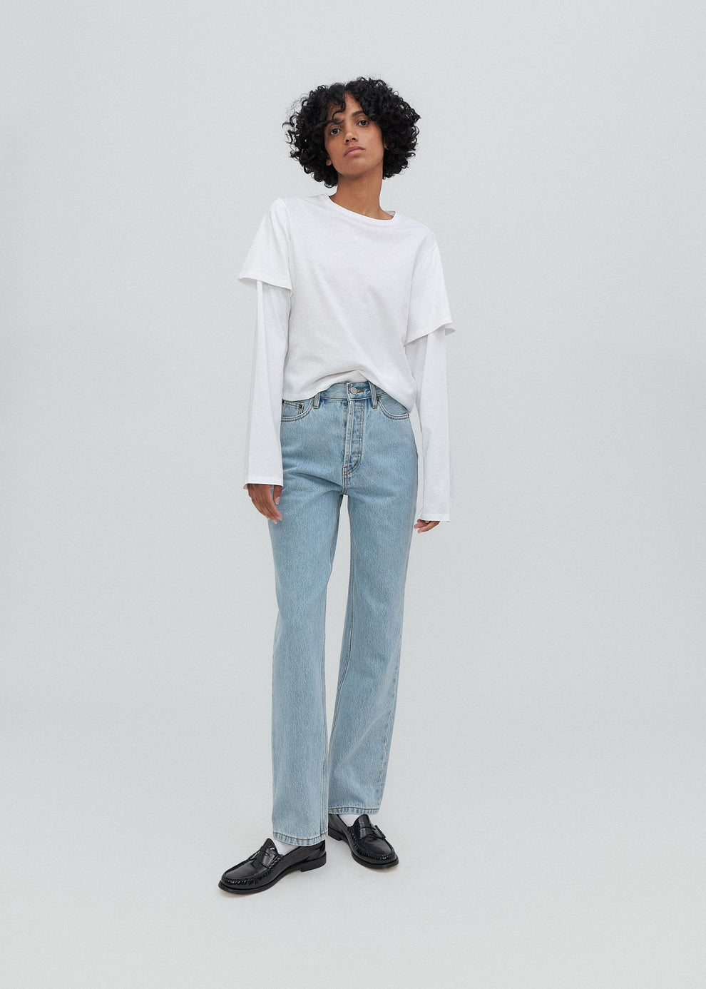 Person wearing a white top and light blue jeans on a plain background