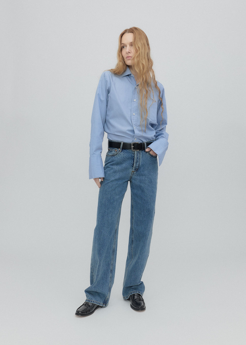 Person wearing a light blue shirt and jeans on a plain background
