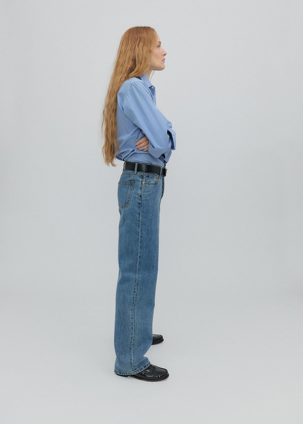Person wearing a light blue shirt and jeans standing against a plain background
