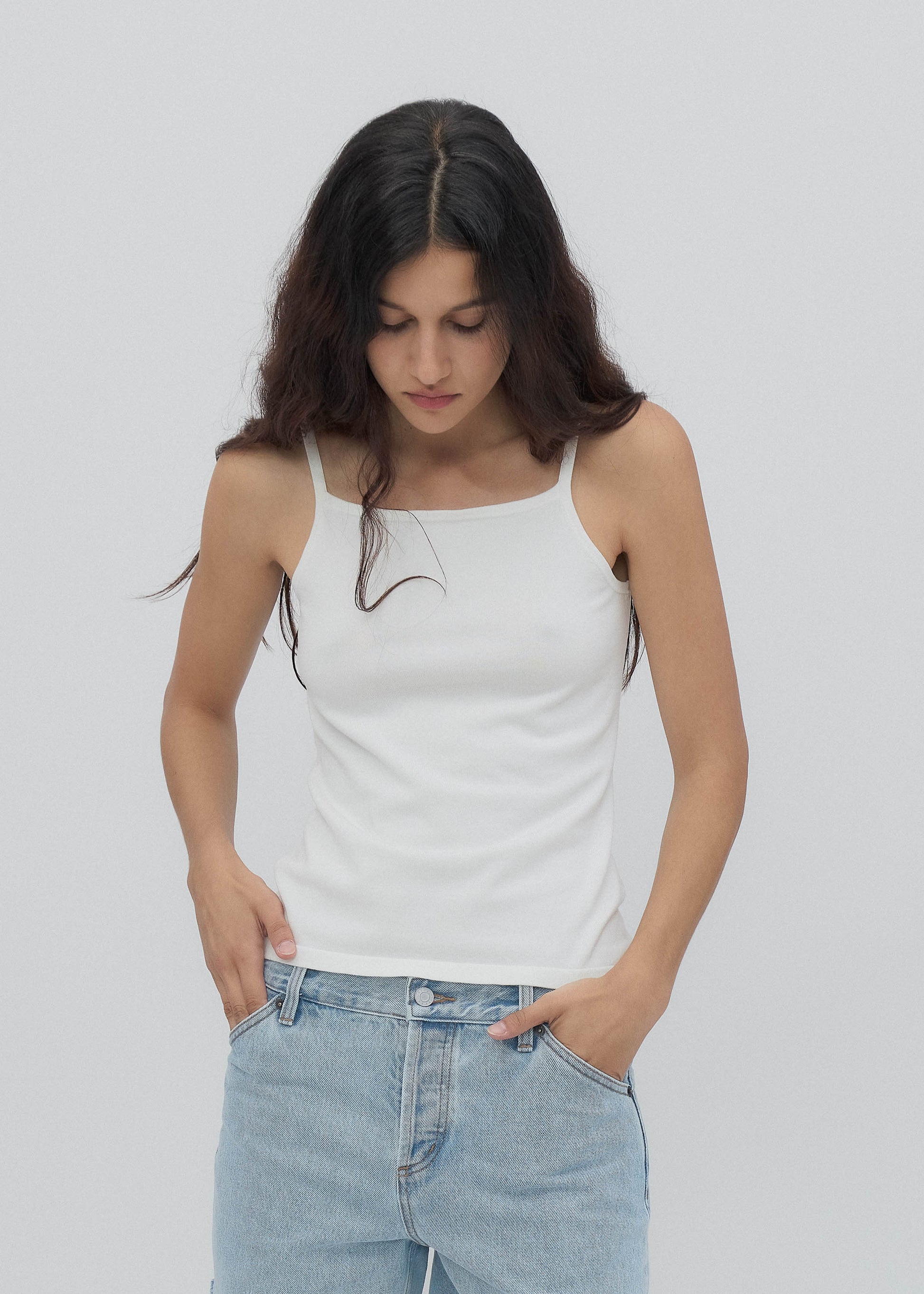 Woman wearing a white tank top and blue jeans against a plain background