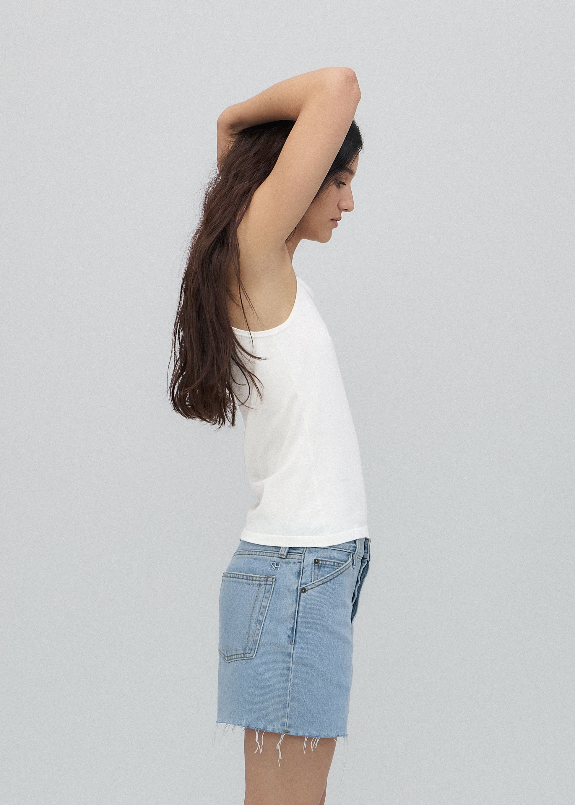 Woman wearing a white top and denim skirt against a plain background