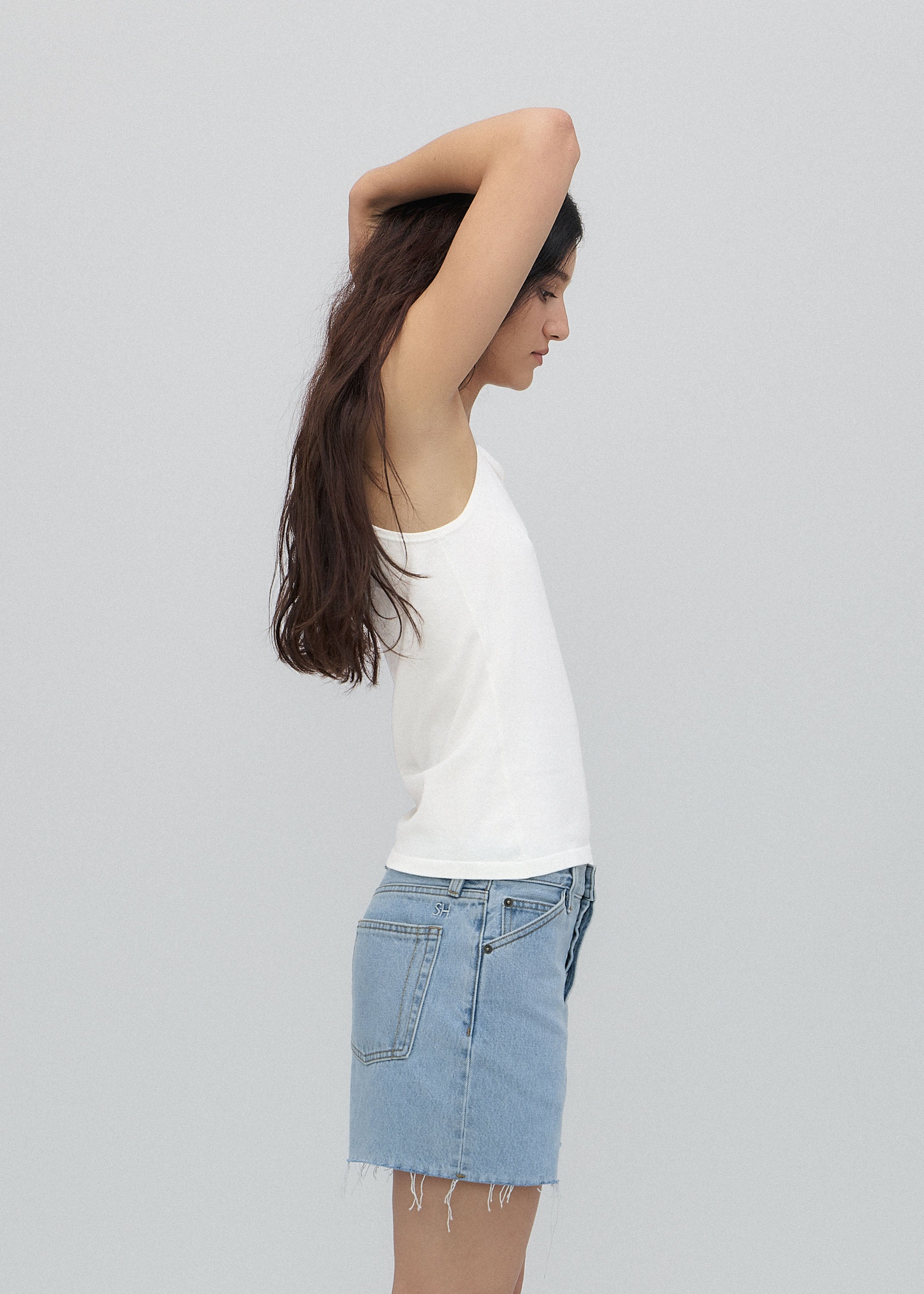 Woman wearing a white top and denim skirt against a plain background