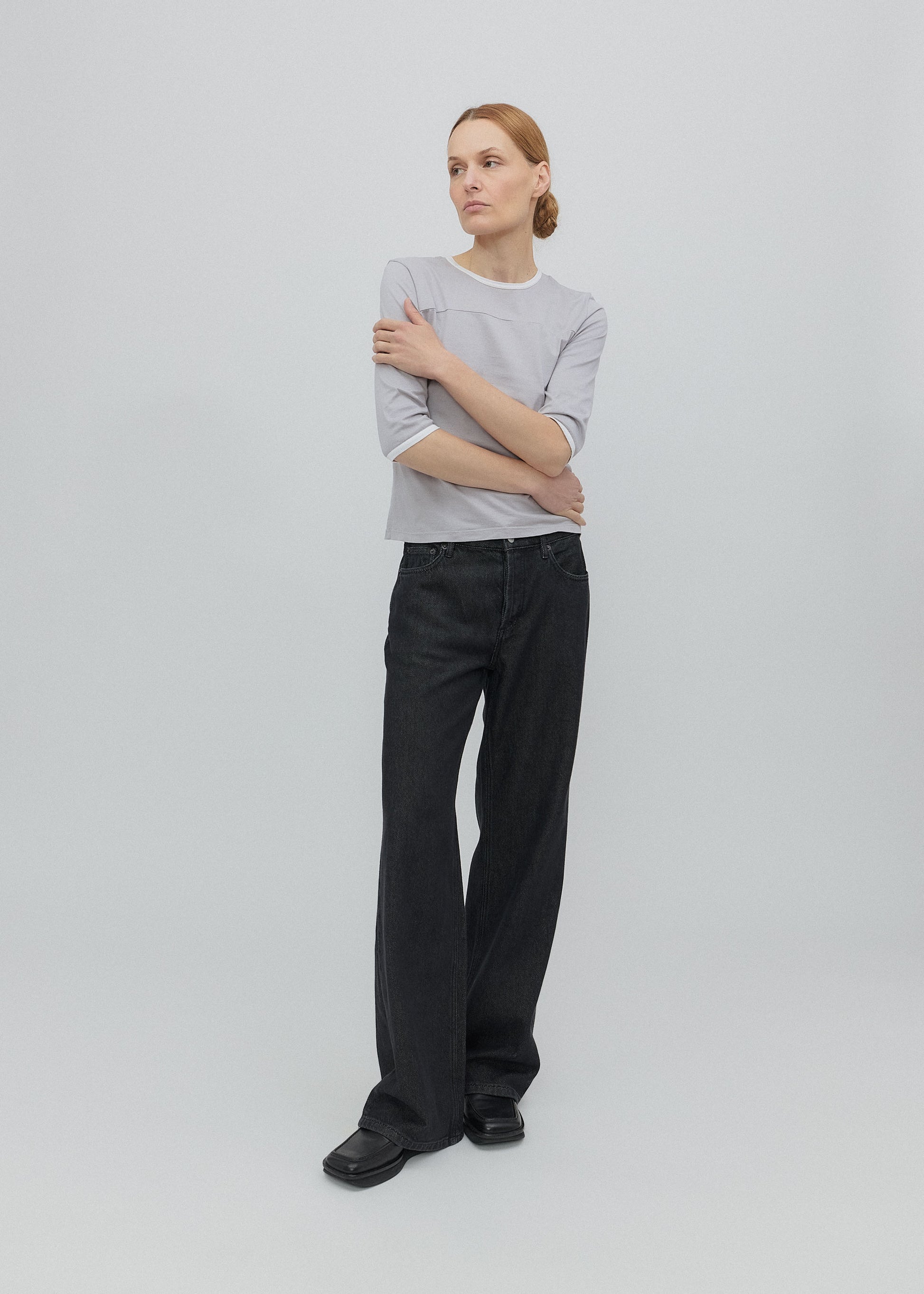 Person wearing a light gray sweater and black pants on a white background