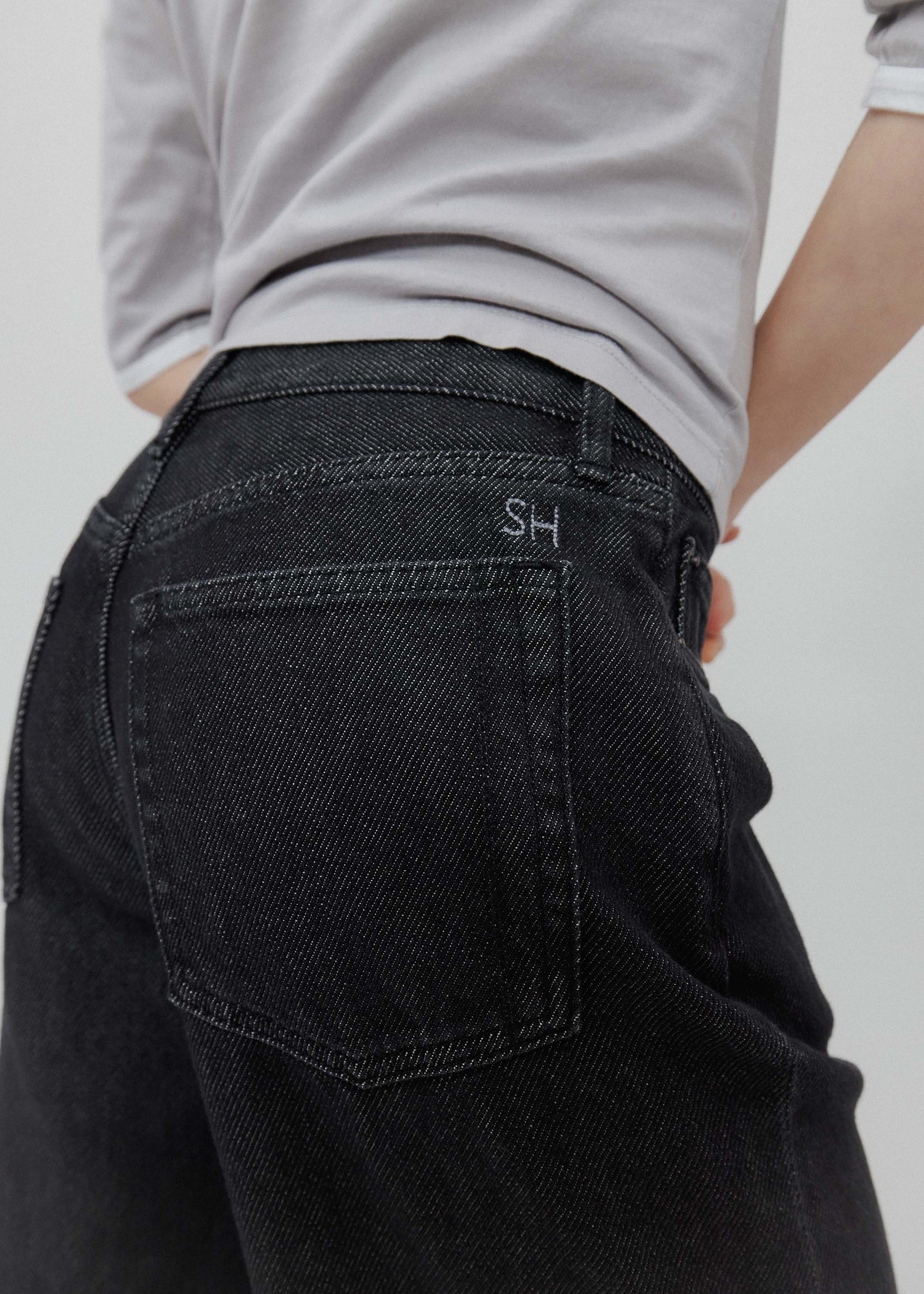 Person wearing black jeans with a visible brand logo on a plain background