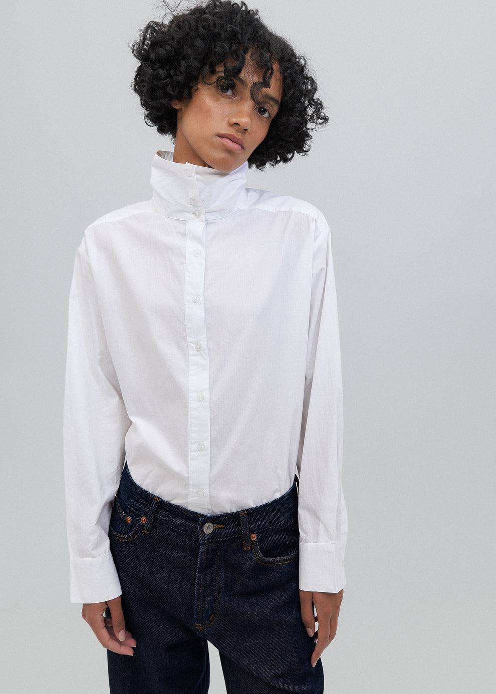 Person wearing a white shirt and dark jeans against a gray background