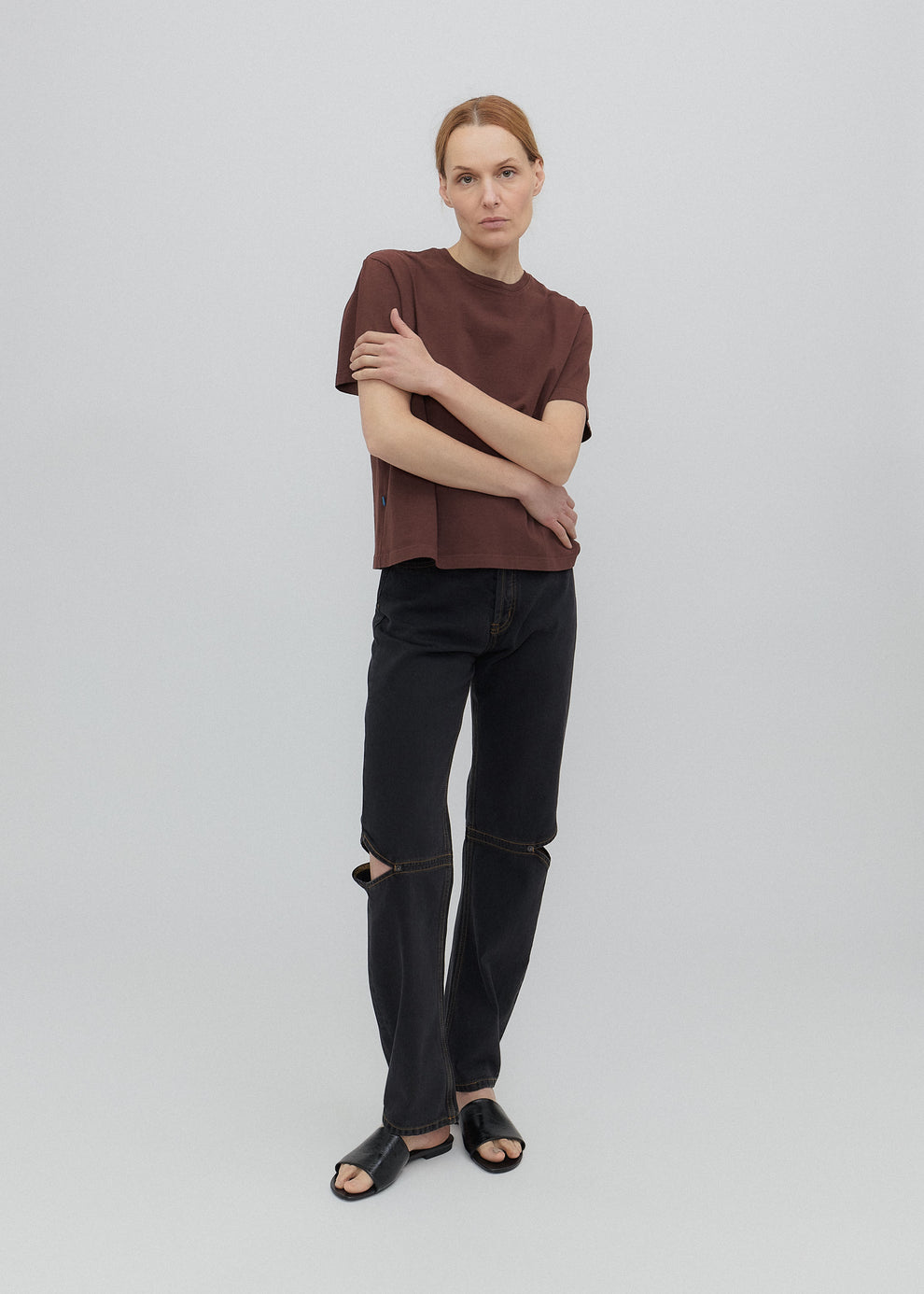 Person wearing a brown top and black jeans on a light gray background