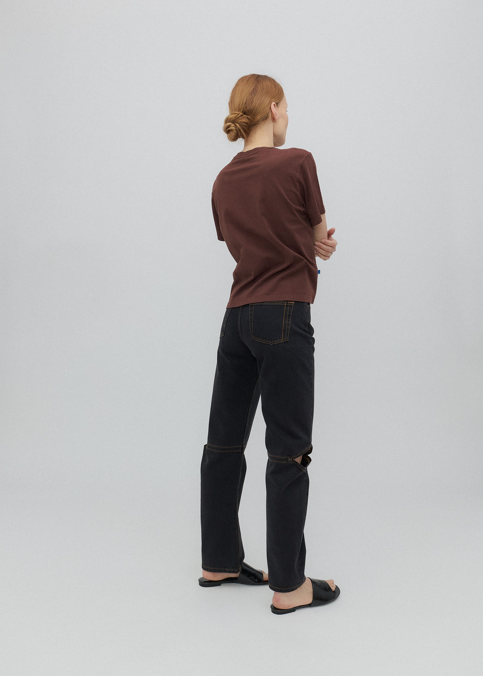 Person wearing a brown shirt and black jeans against a white background