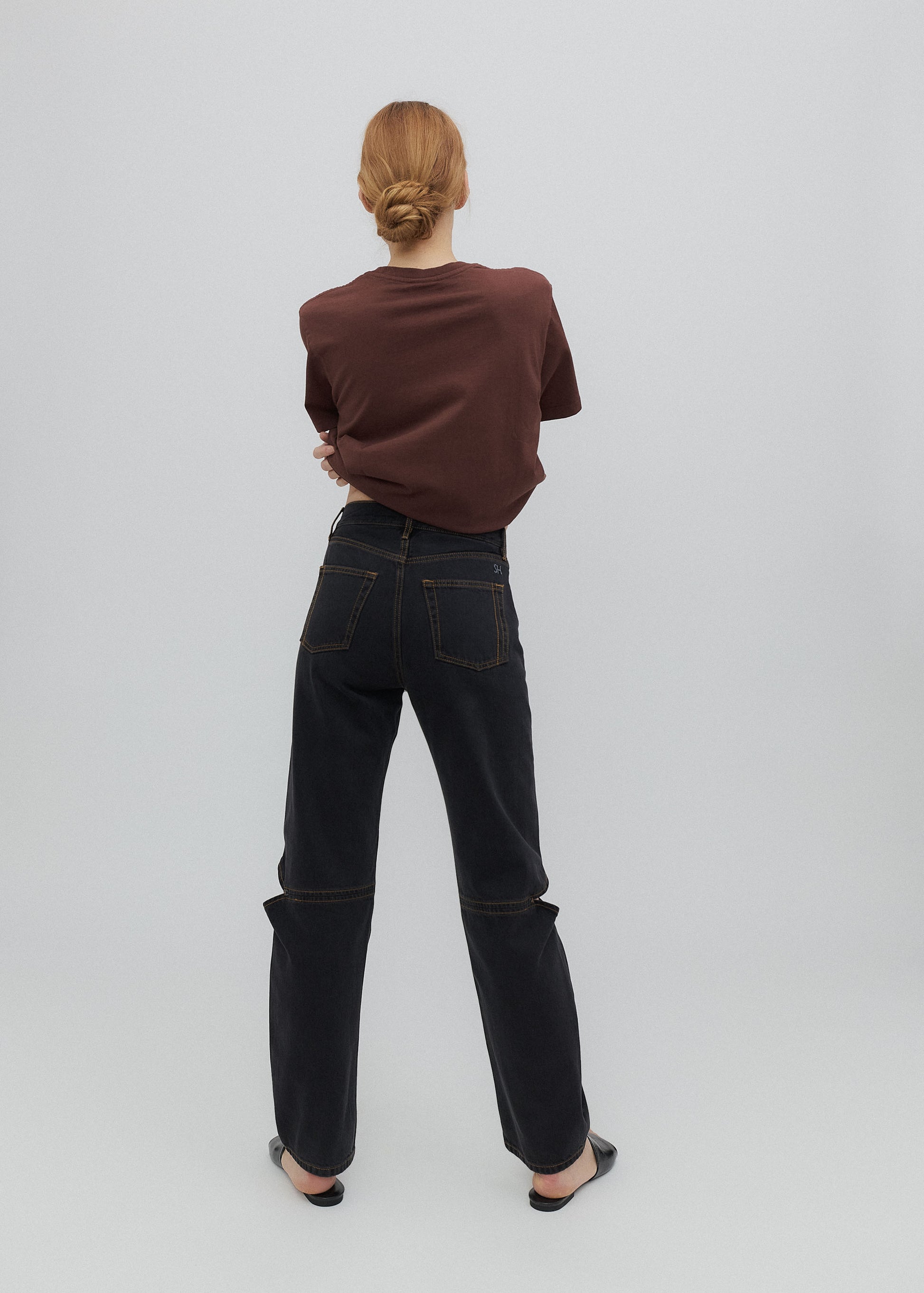 Person wearing a brown sweater and black jeans on a white background