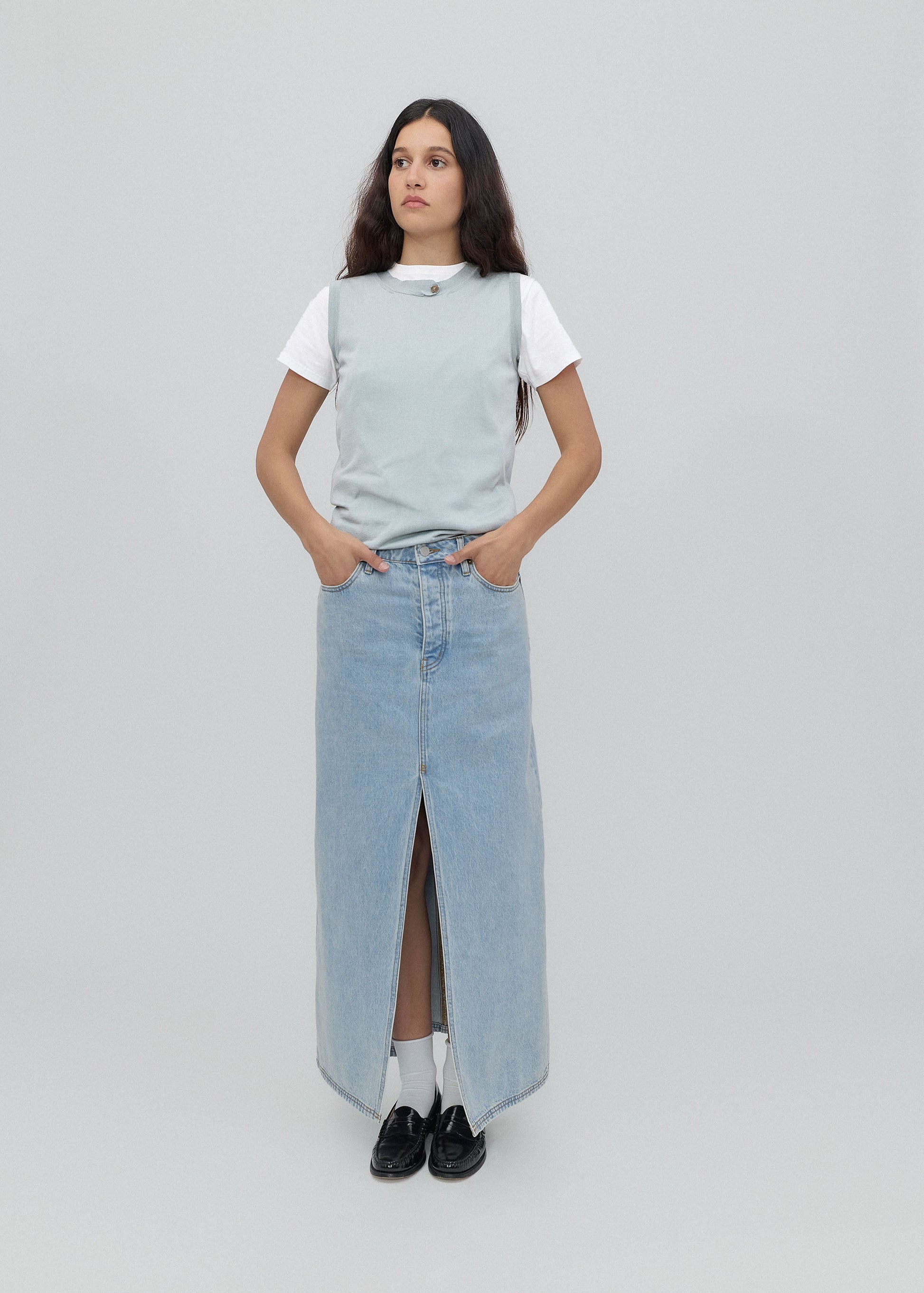 Woman wearing a light gray sleeveless top and denim skirt on a plain background