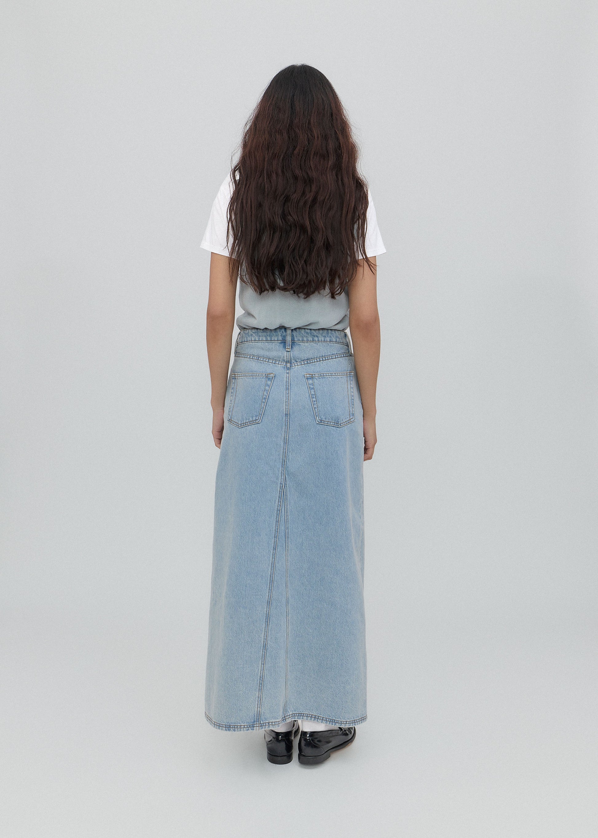 Person wearing a light blue denim skirt on a plain background