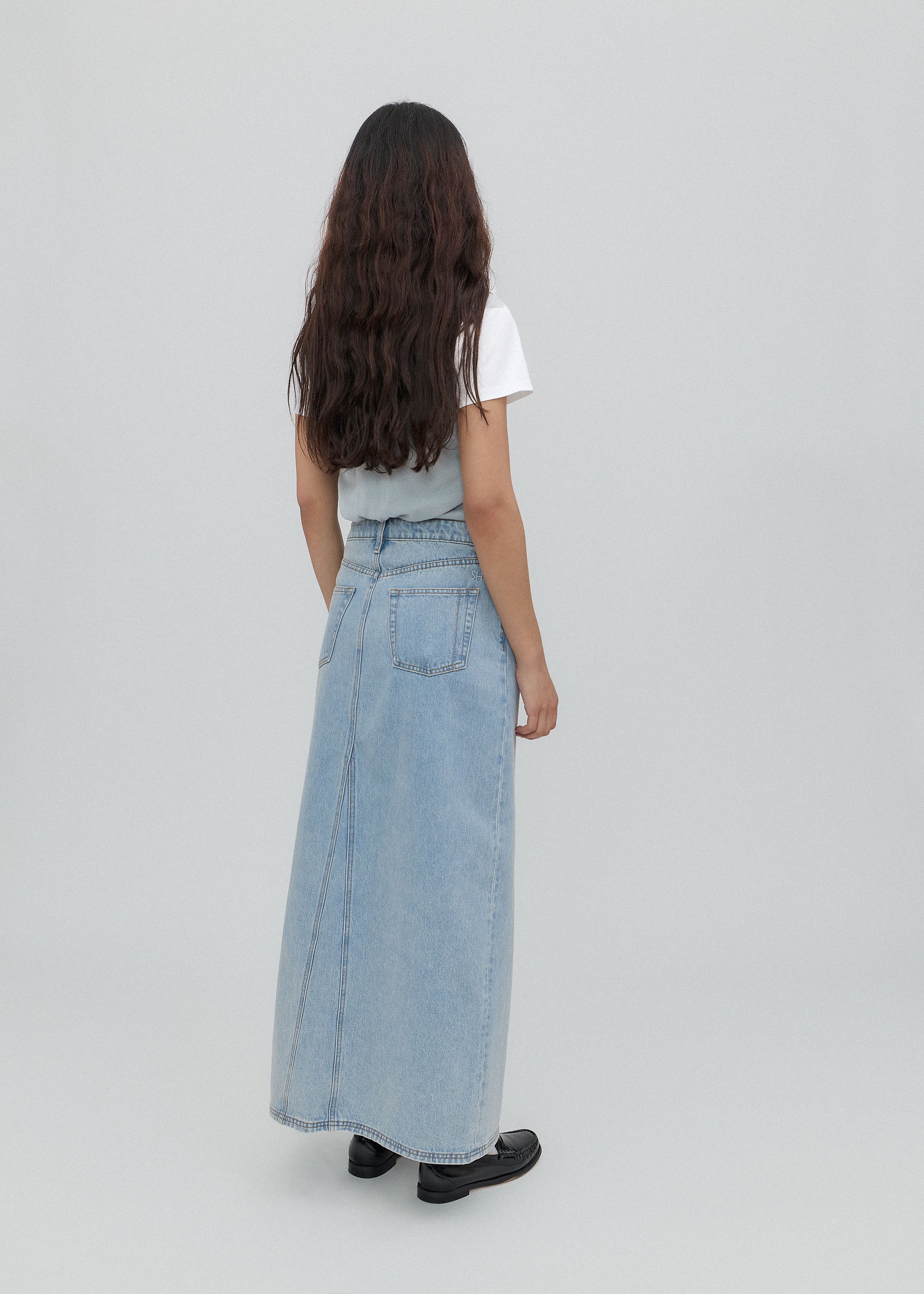 Person wearing a light blue denim skirt and white top on a plain background