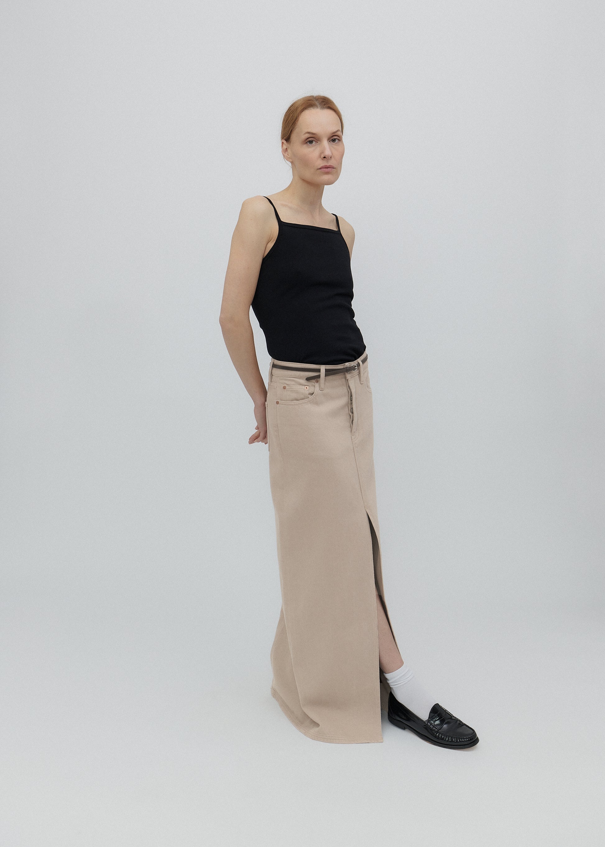 Woman wearing a black tank top and beige pants on a white background