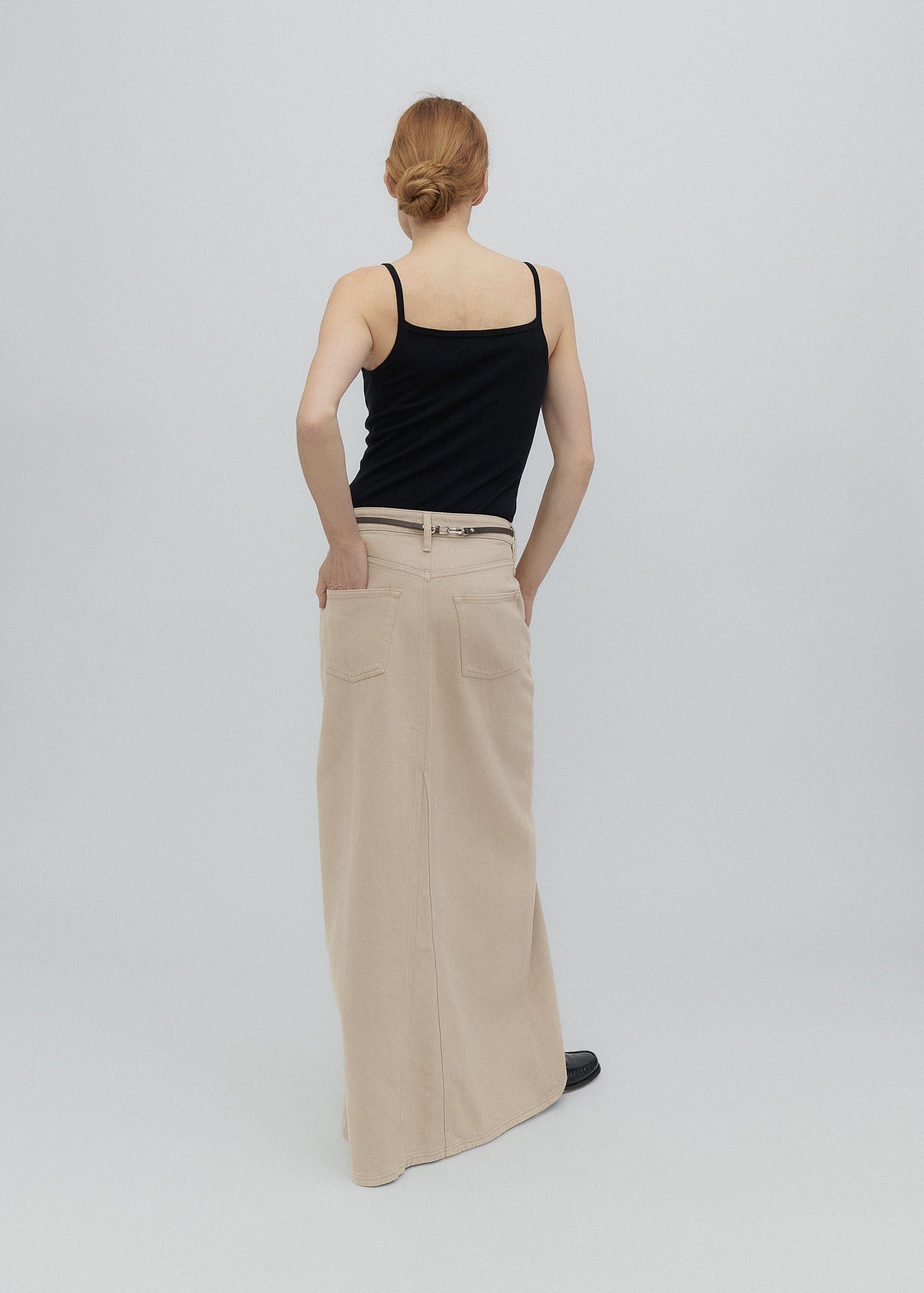 Person wearing a black tank top and beige wide-leg pants on a light gray background