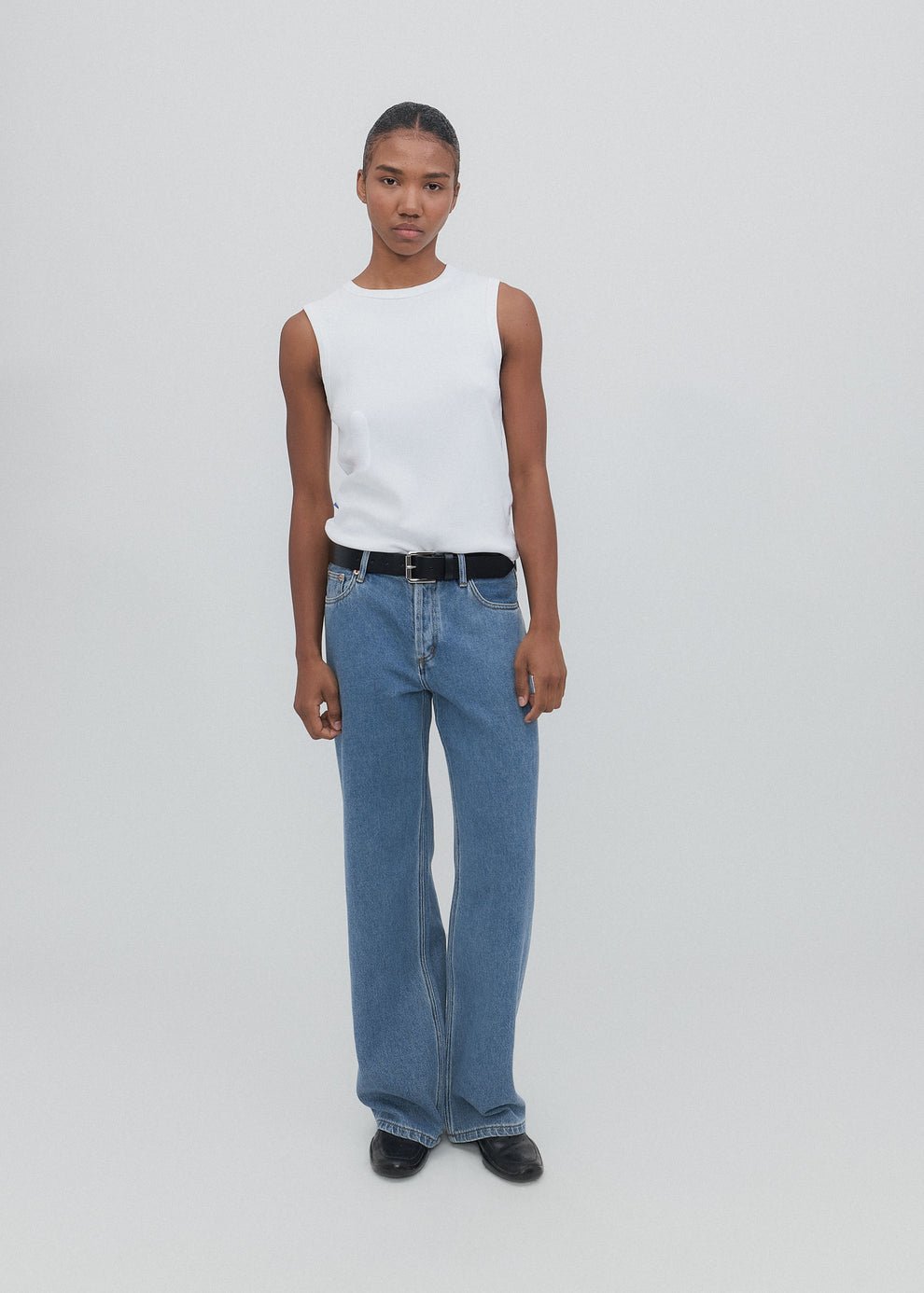 Person wearing a white sleeveless top and blue jeans on a plain background