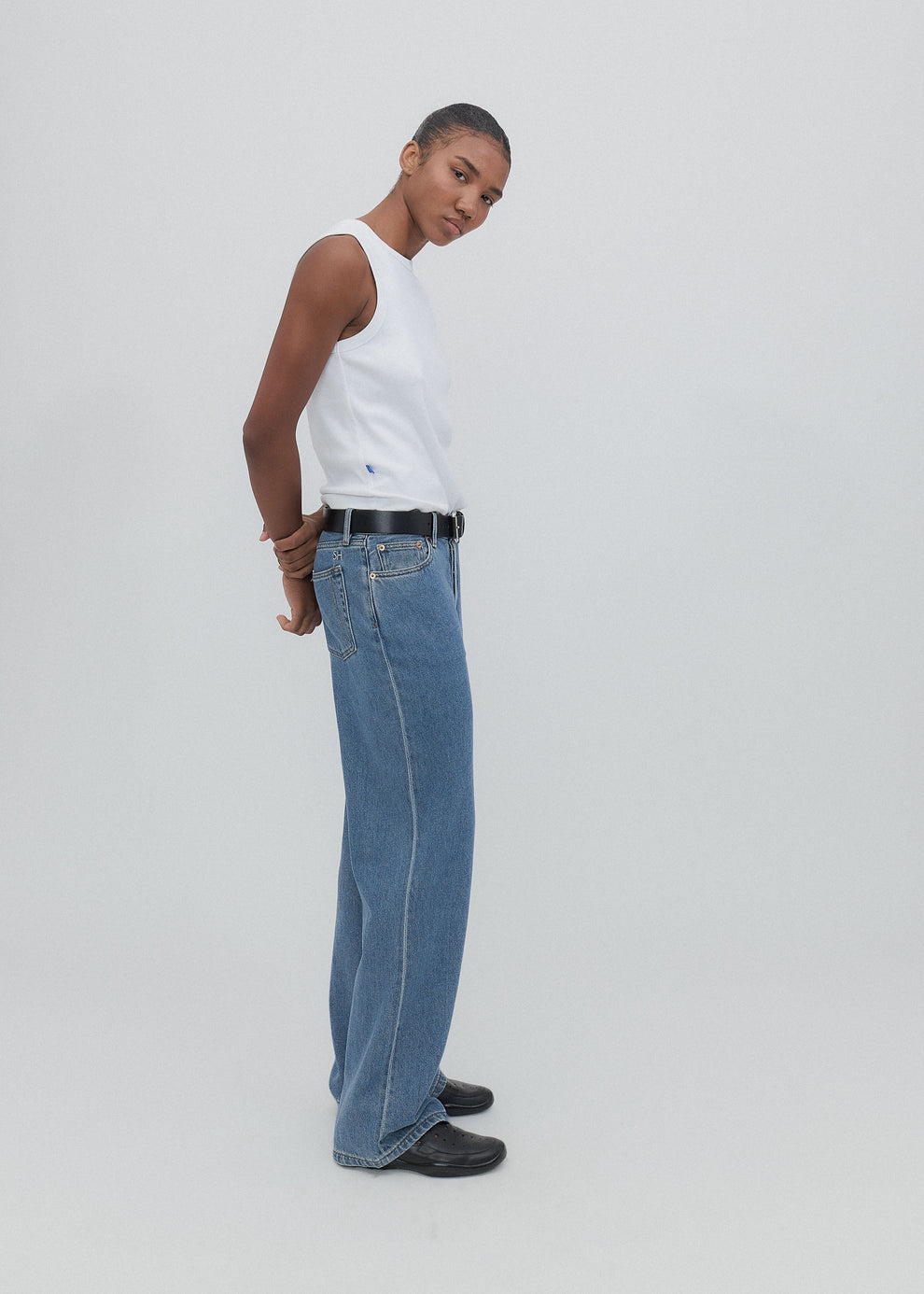 Person wearing a white sleeveless top and blue jeans on a plain background
