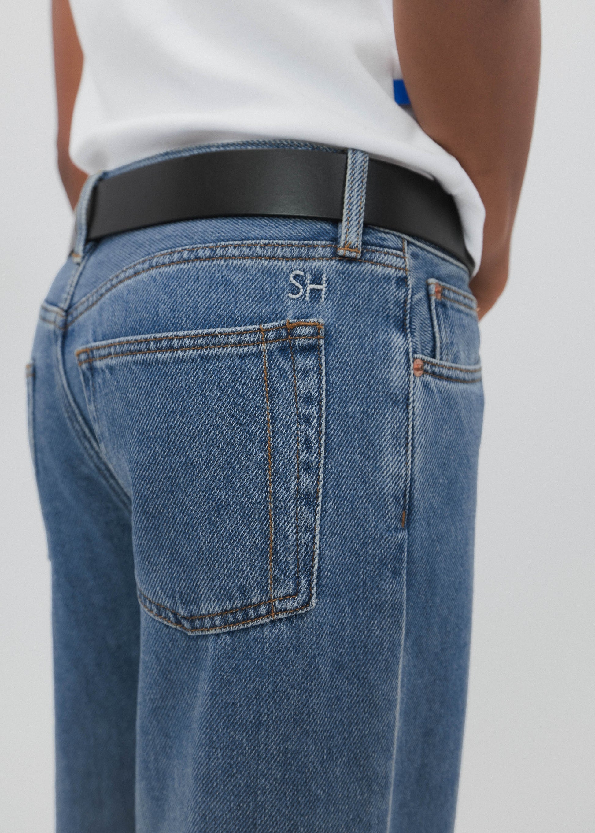 Person wearing blue jeans with a visible brand logo on a plain background