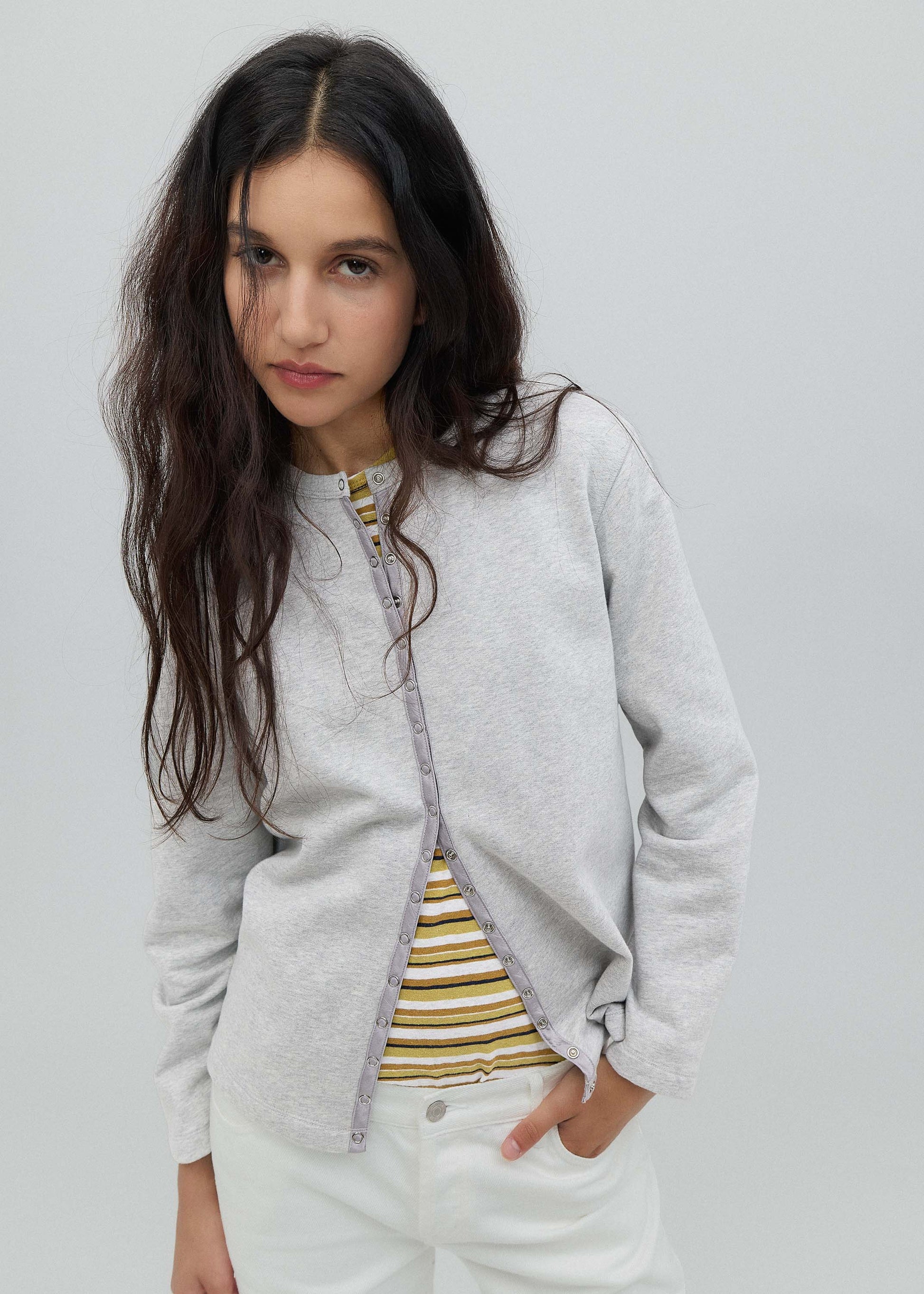 Woman wearing a light gray cardigan over a striped shirt on a plain background