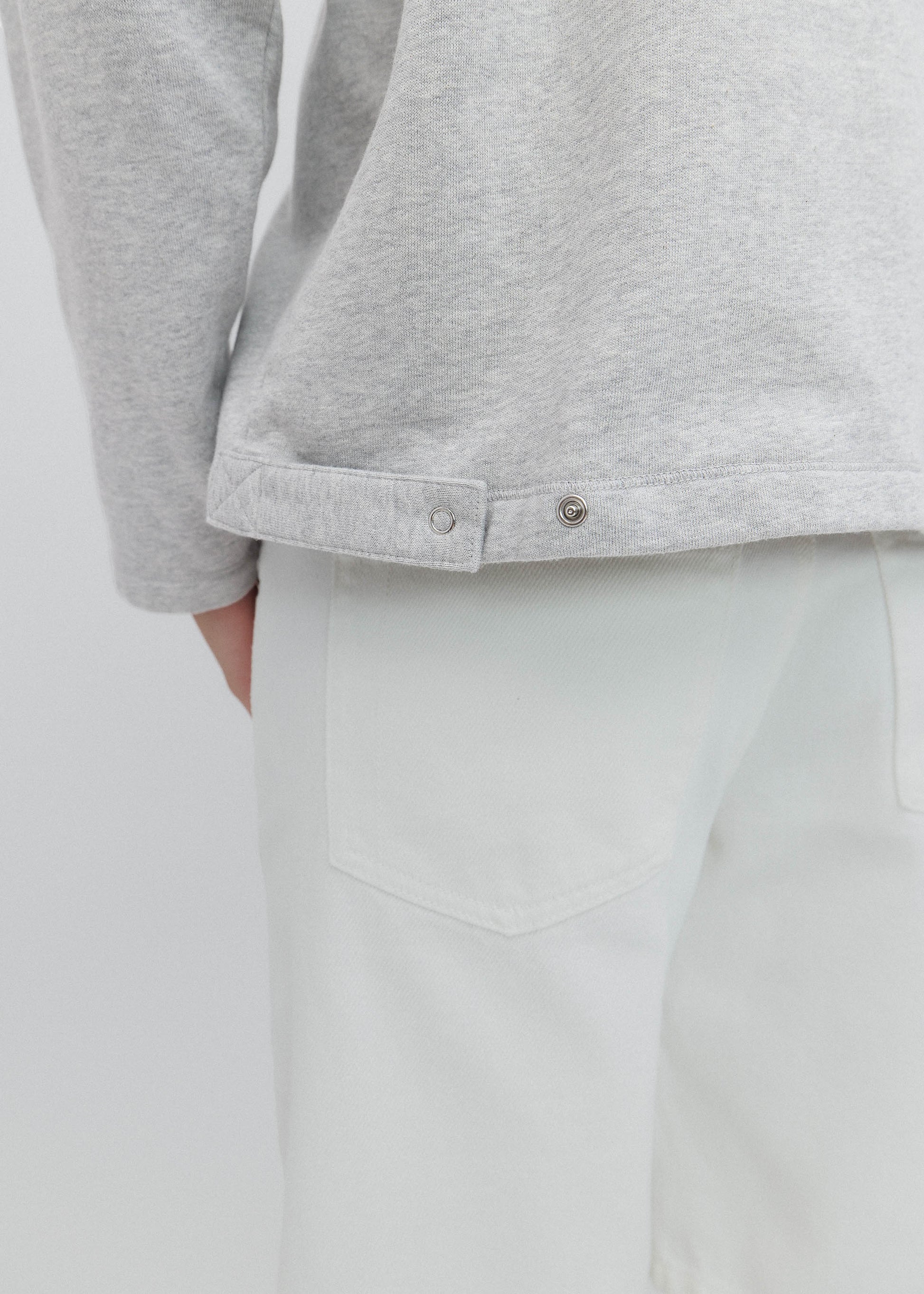 Close-up of a person wearing a gray long-sleeve shirt and light gray pants on a plain background